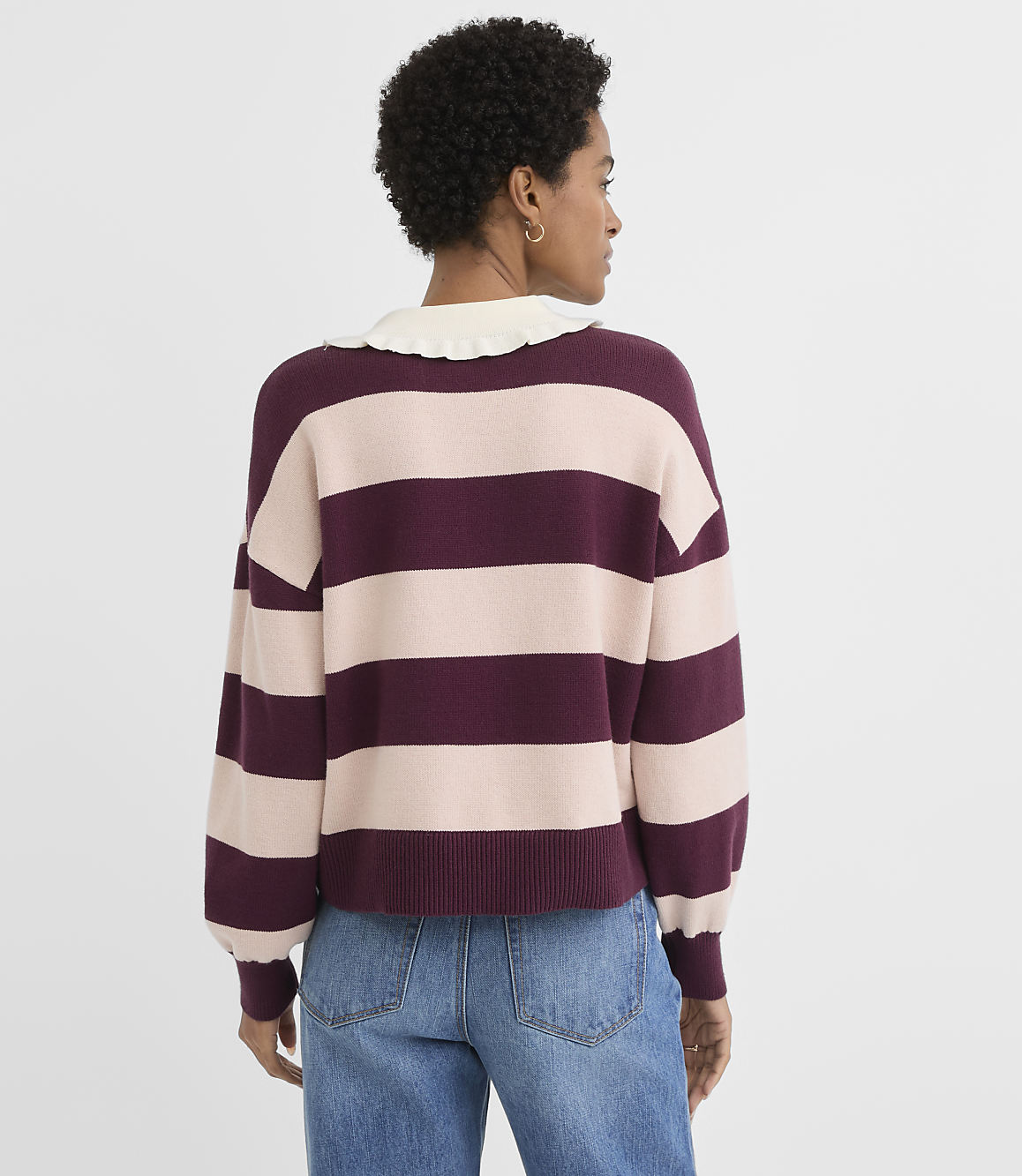 A woman in a striped sweater and jeans stands against a plain white background.