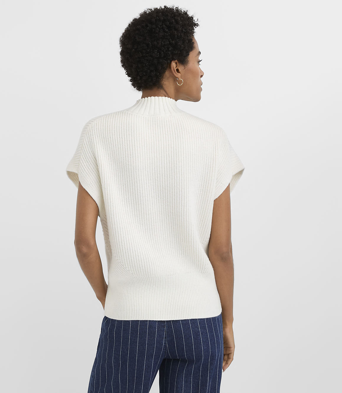 A woman in a cream ribbed sweater and navy pinstripe pants stands against a plain white background.