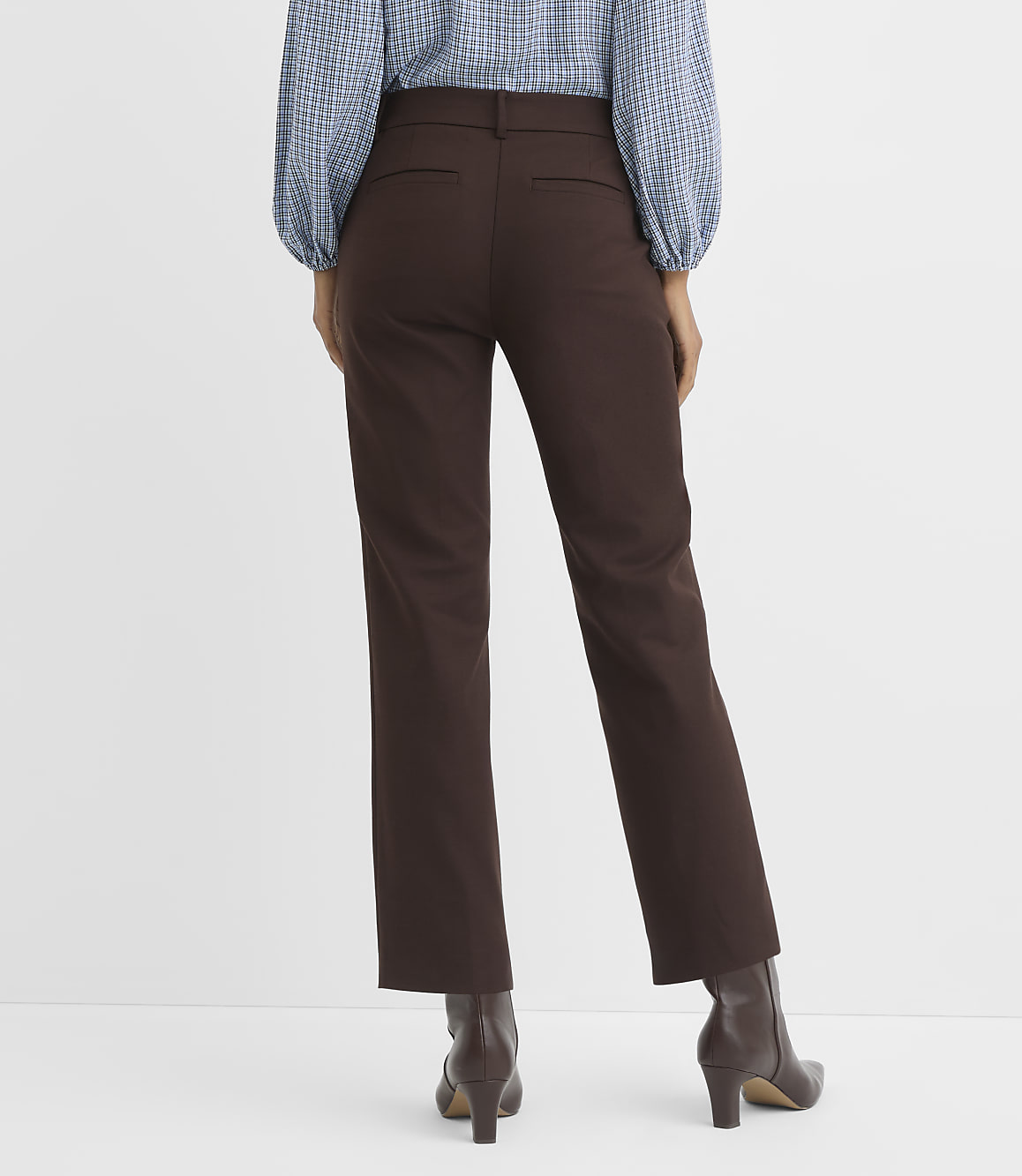 A person wearing brown pants and a blue patterned shirt stands against a plain white background.