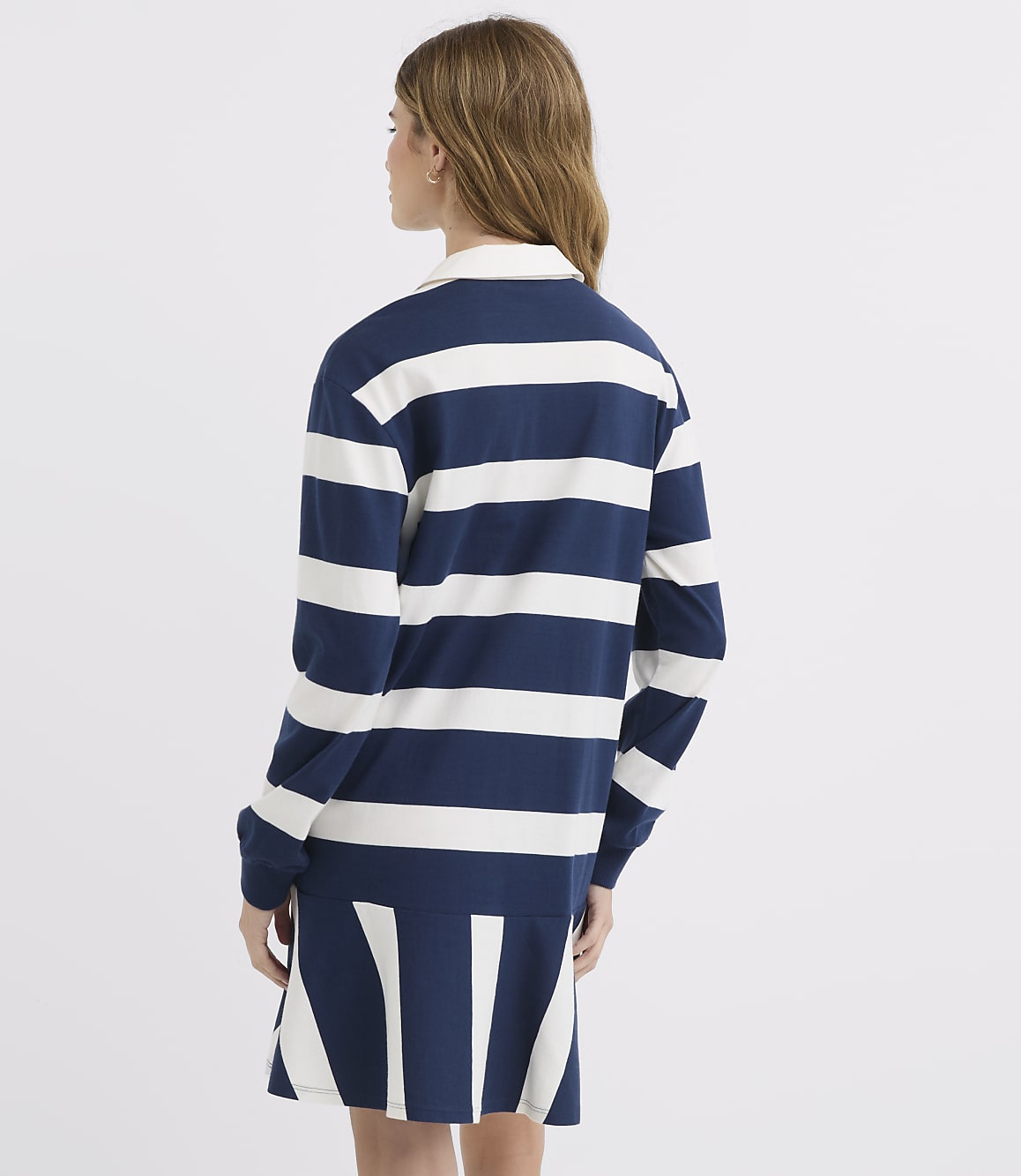 A young woman in a navy and white striped rugby dress stands against a plain white background.