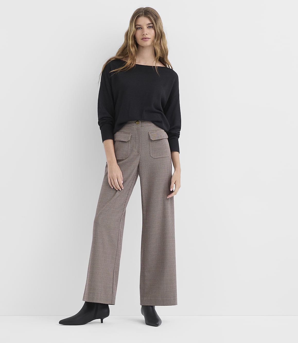 A woman in a black sweater and patterned wide-leg pants stands against a plain white background.