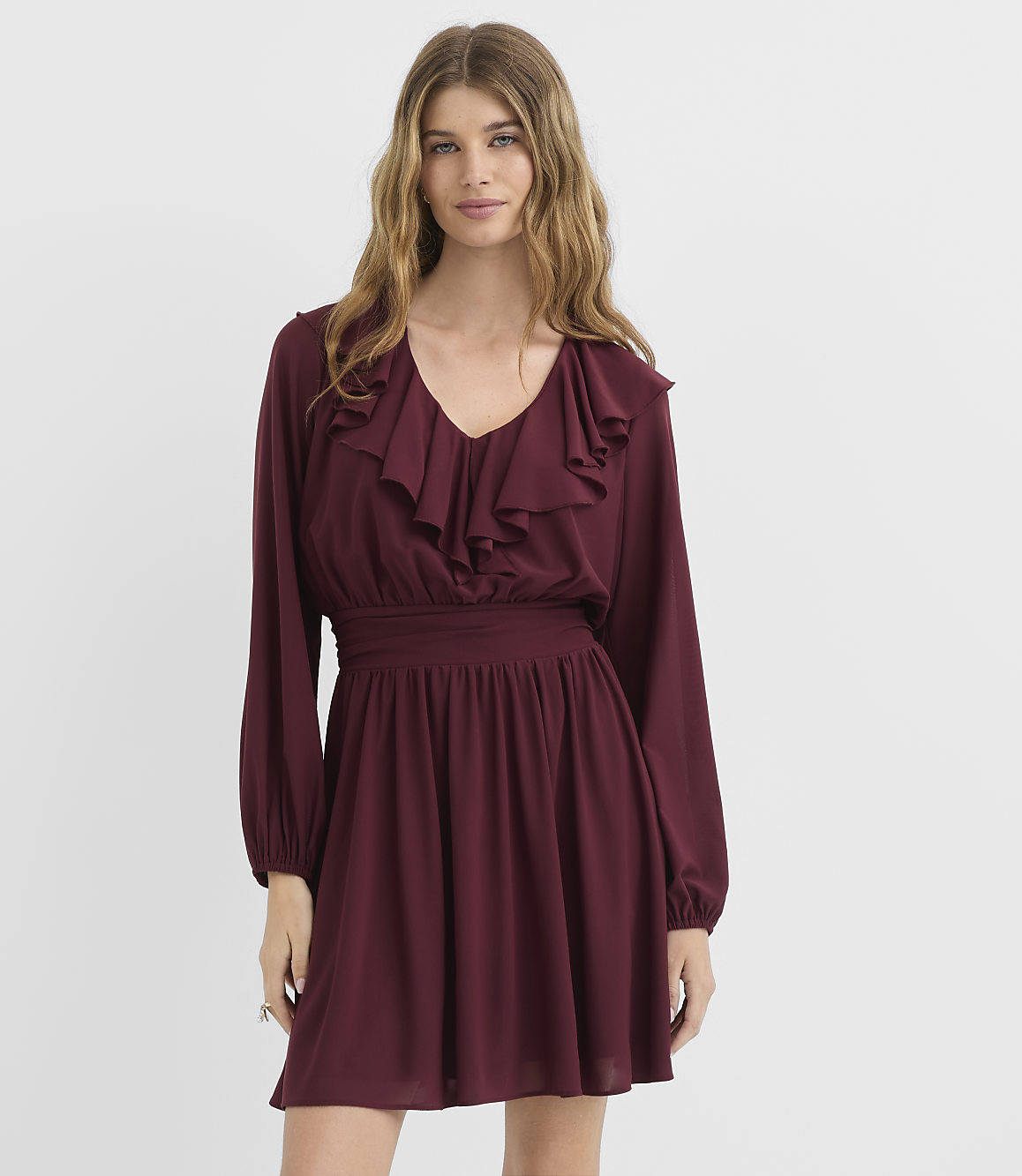 A woman in a burgundy ruffled dress stands against a plain white background.