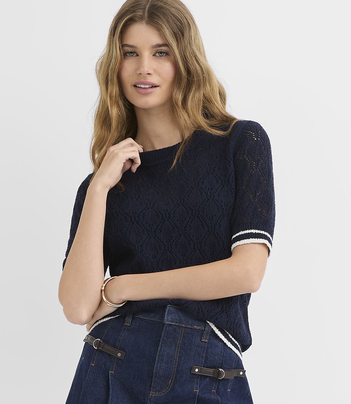 A woman in a navy blue knit top and denim shorts poses against a plain white background.