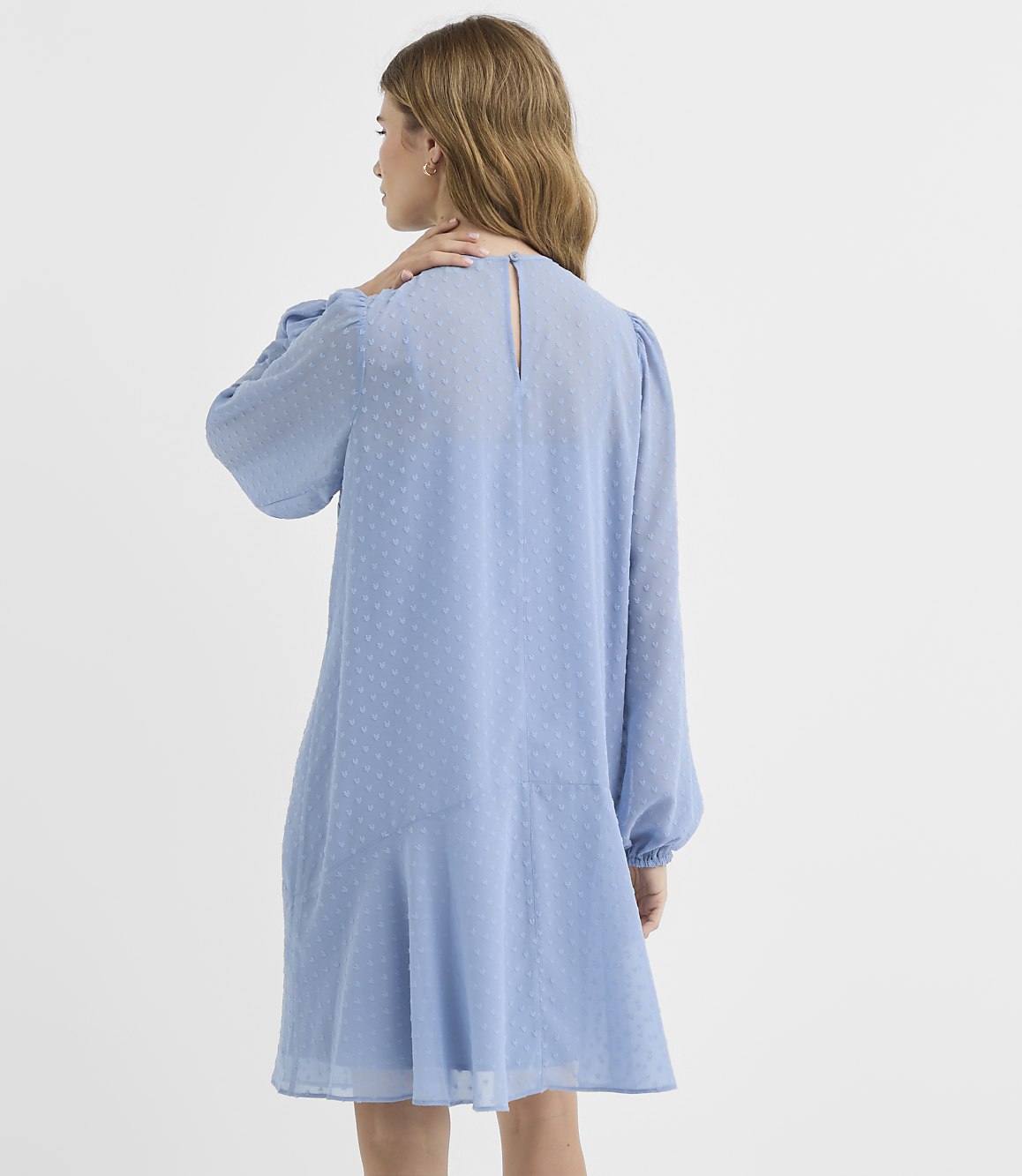 A woman in a light blue, textured dress stands against a plain white background.