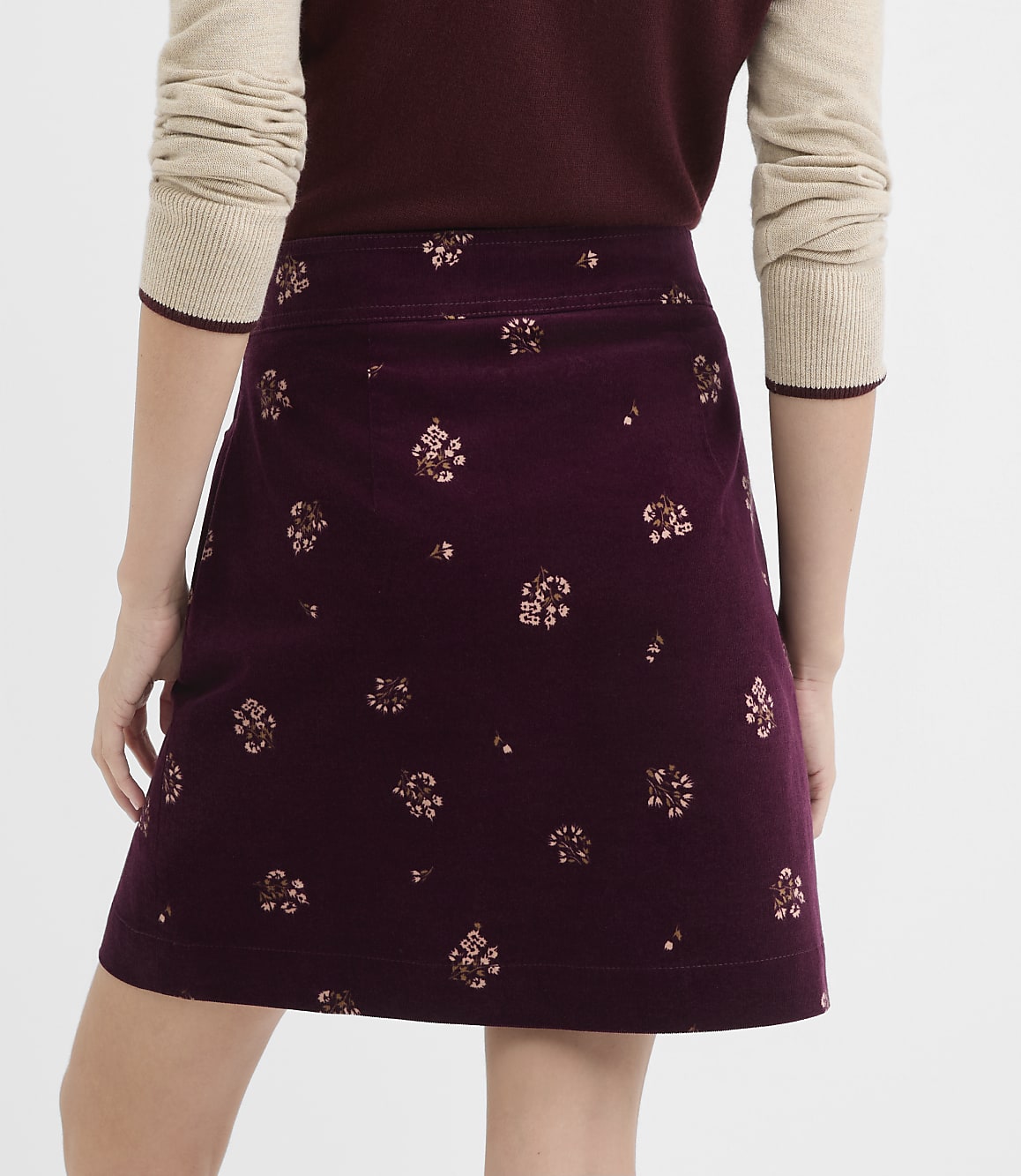 A person wearing a burgundy A-line skirt with a floral pattern stands against a plain white background.