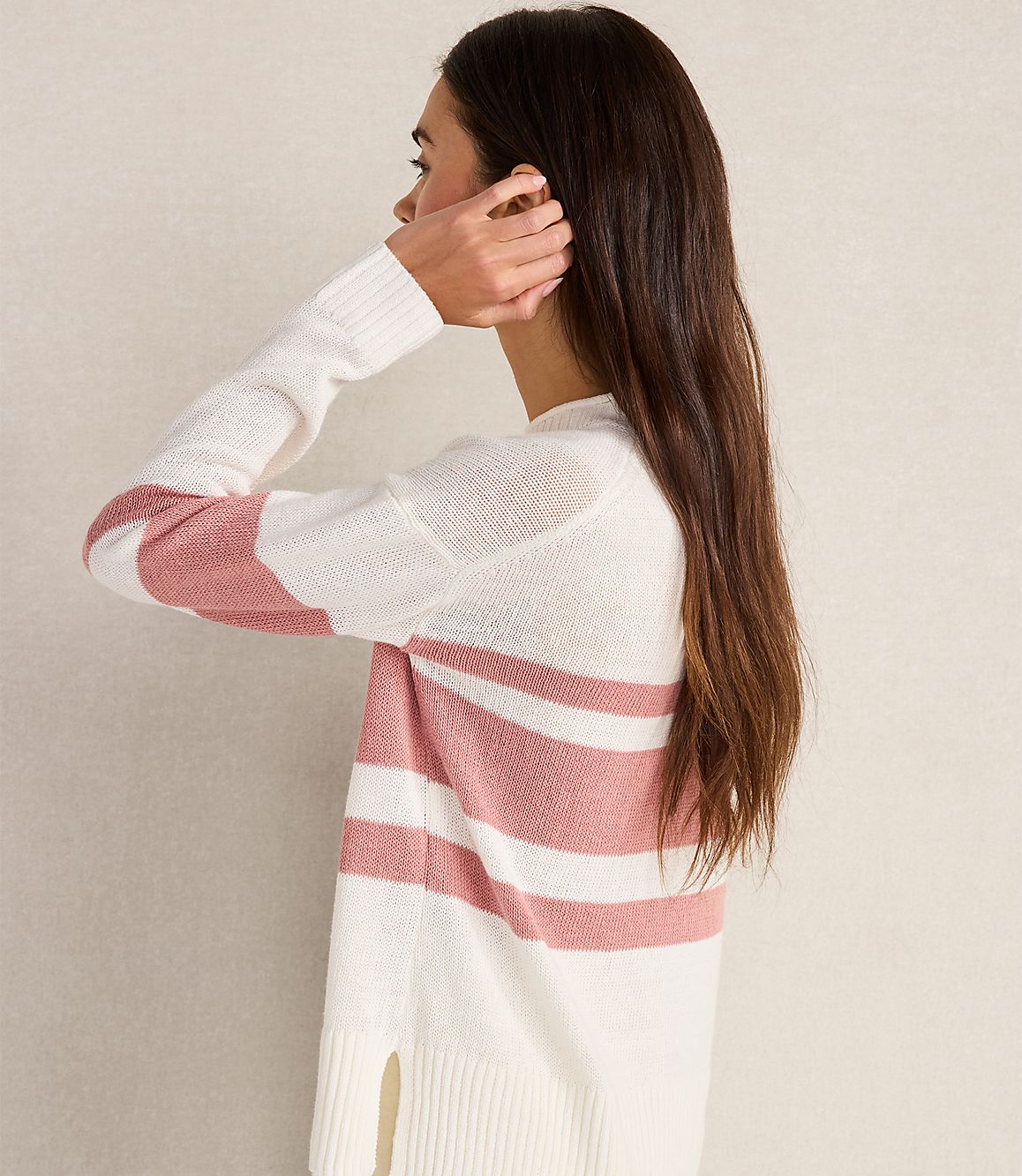 A woman in a striped sweater stands against a plain, light-colored background.