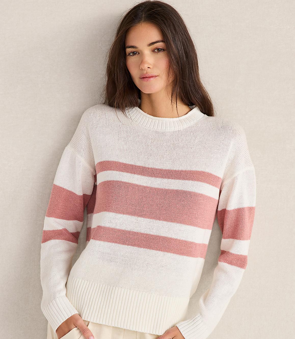 A woman in a striped sweater stands against a plain, light-colored wall.