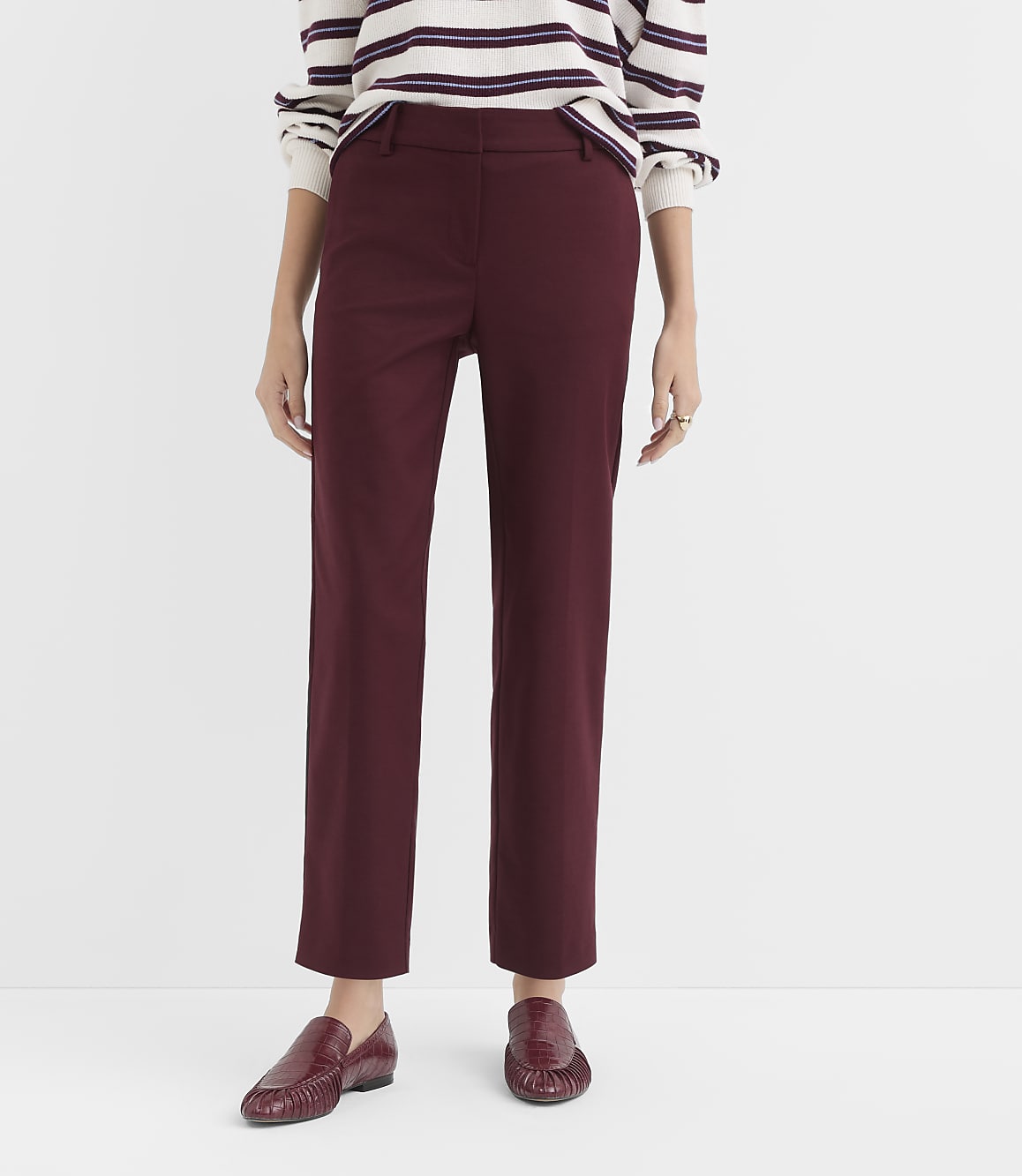 A person wearing burgundy pants and matching loafers stands against a plain white background.