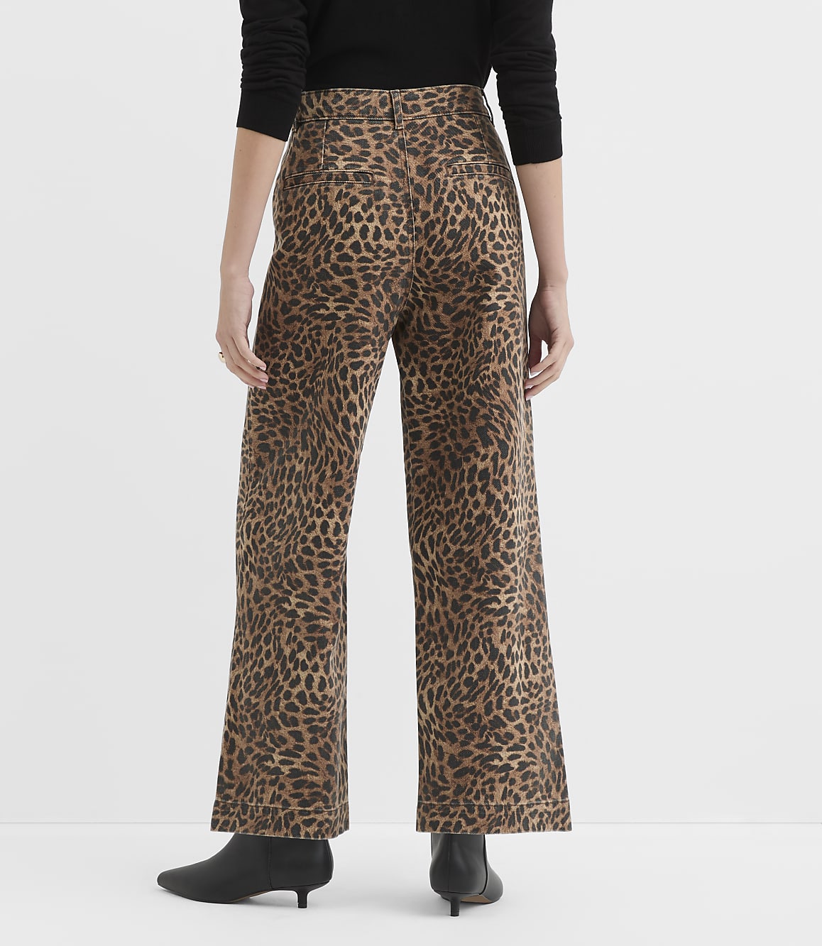 A person wearing leopard-print wide-leg pants and black boots stands against a plain white background.