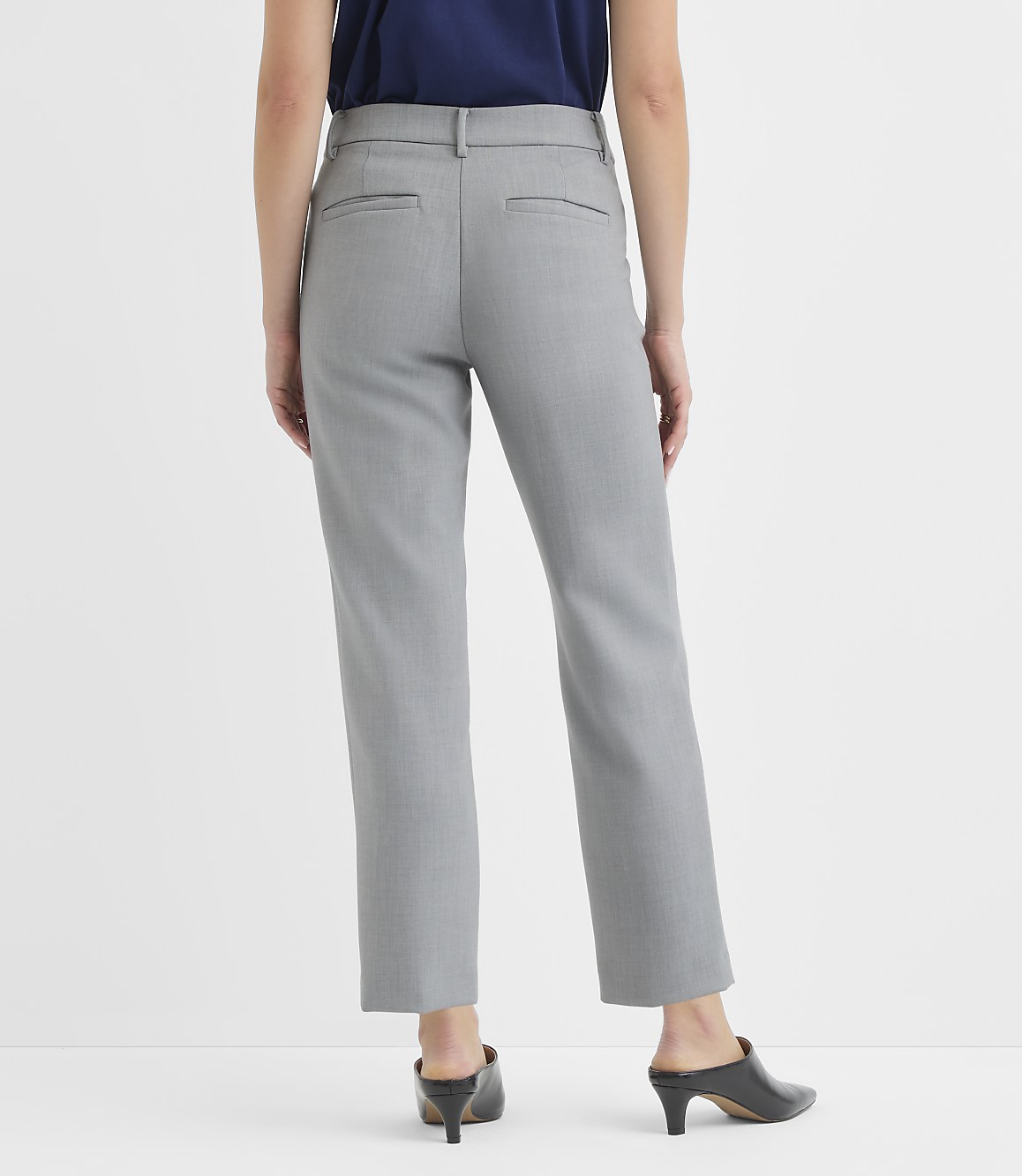 A person wearing gray pants and a navy top stands against a plain white background.