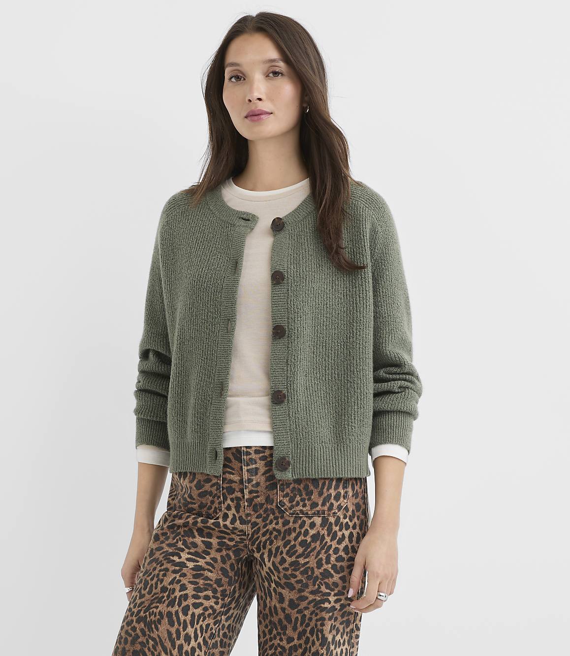 A woman in a green cardigan and leopard print pants stands against a plain white background.
