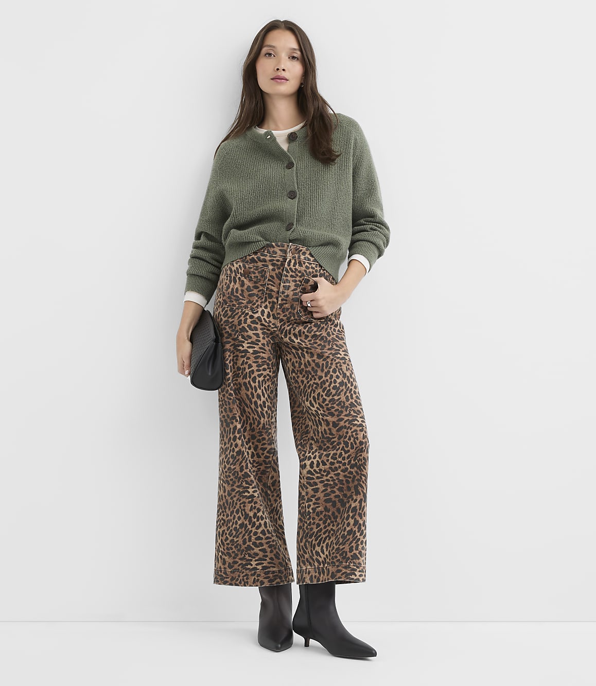 A woman in a green cardigan and leopard print pants stands against a plain white background.