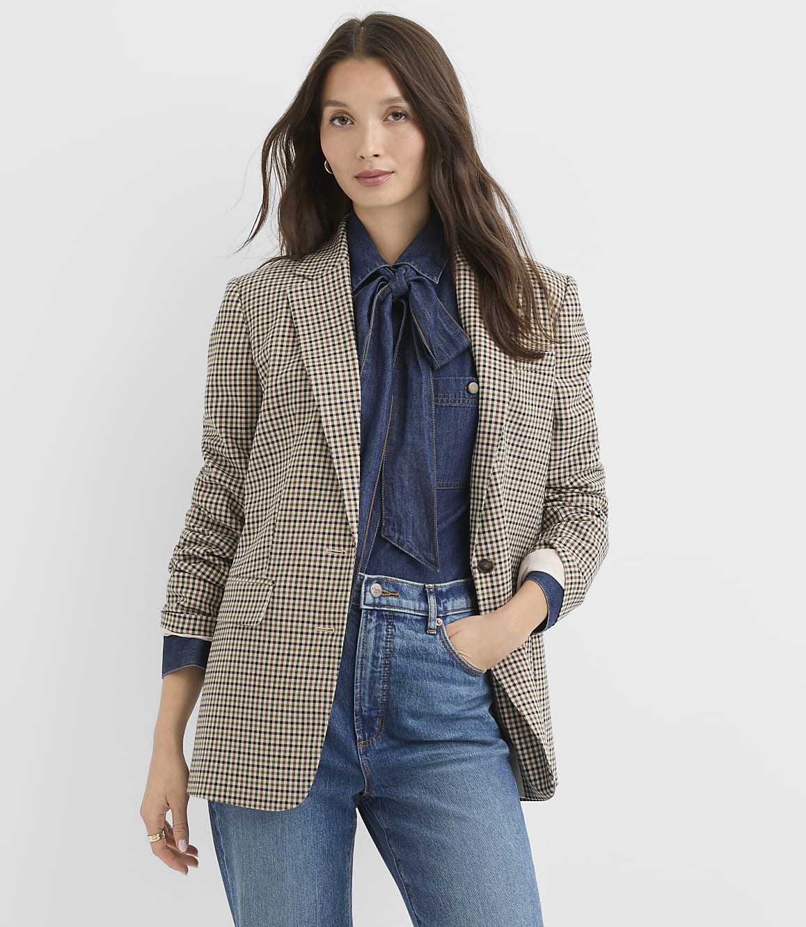 A woman in a patterned blazer and denim shirt stands against a plain white background.