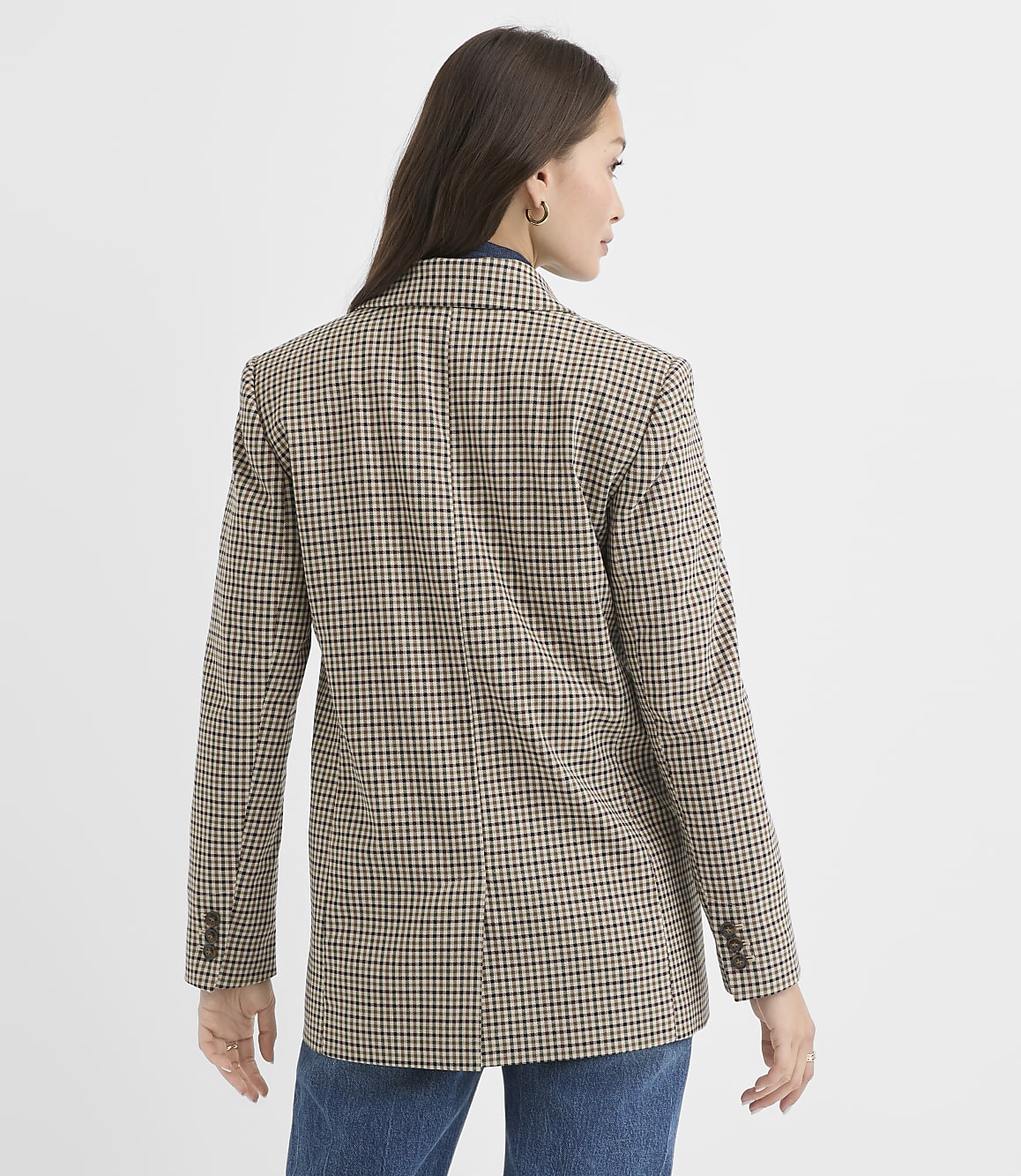 A woman in a brown and white checkered blazer stands against a plain white background.