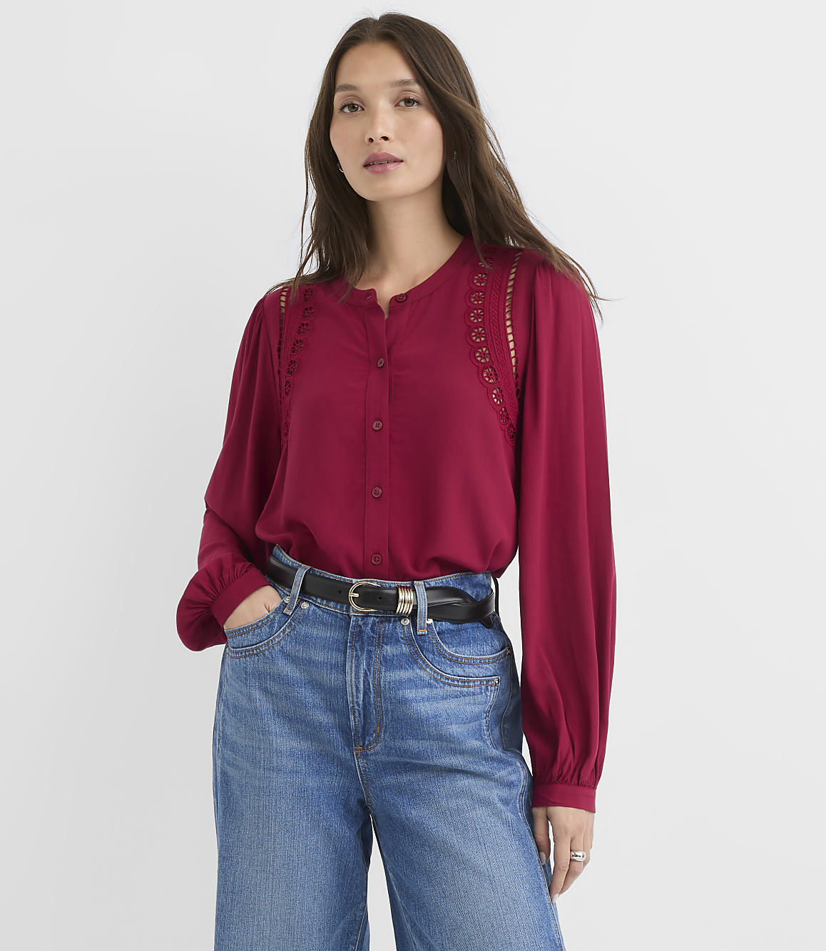 A woman in a maroon blouse and blue jeans stands against a plain white background.