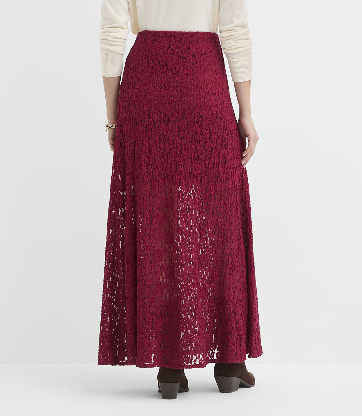 A person wearing a red lace maxi skirt and a cream sweater stands against a plain white background.