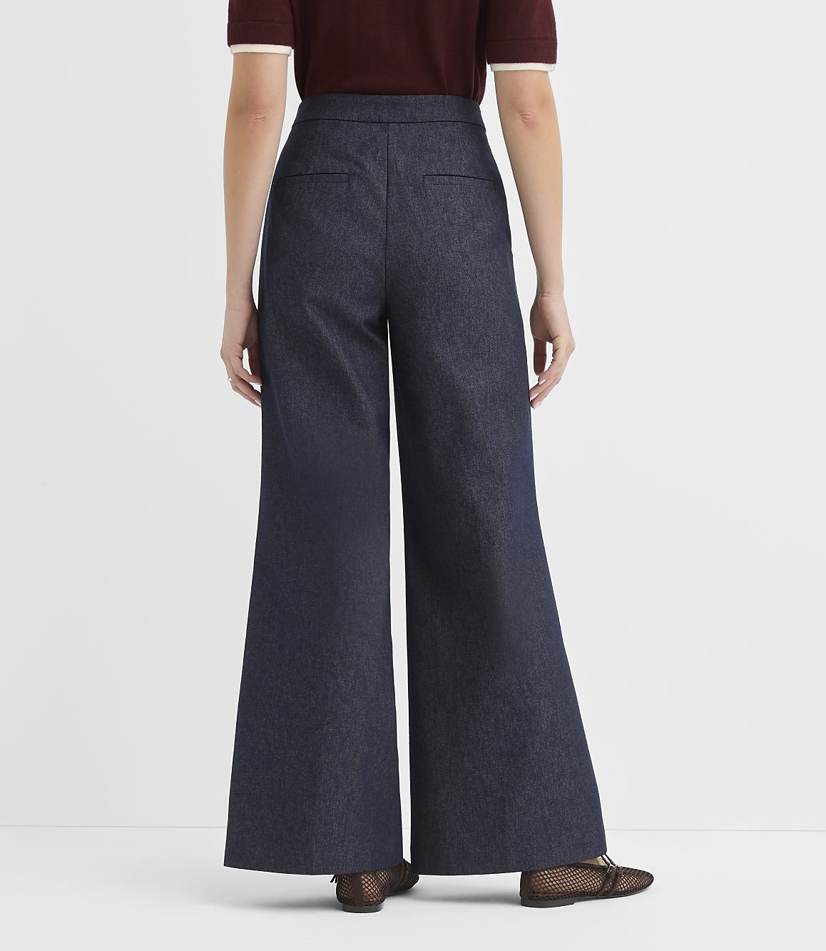 A person wearing dark wash wide-leg denim pants and sheer patterned flats stands against a plain white background.