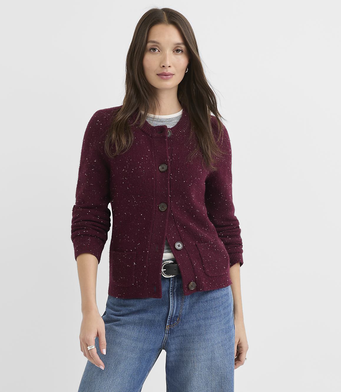 A woman in a burgundy cardigan and jeans stands against a plain white background.