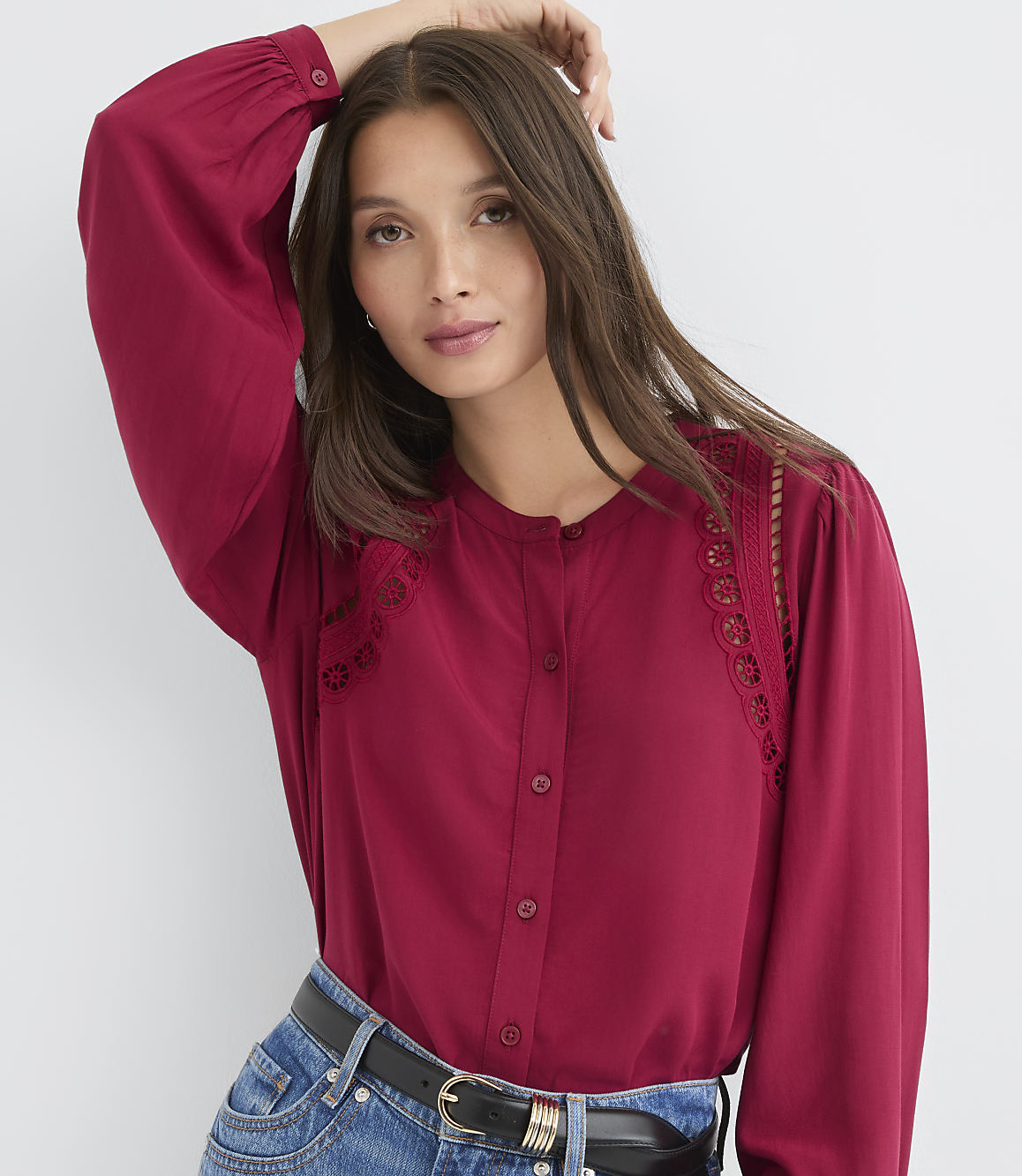 A woman in a maroon blouse and jeans poses against a plain white background.