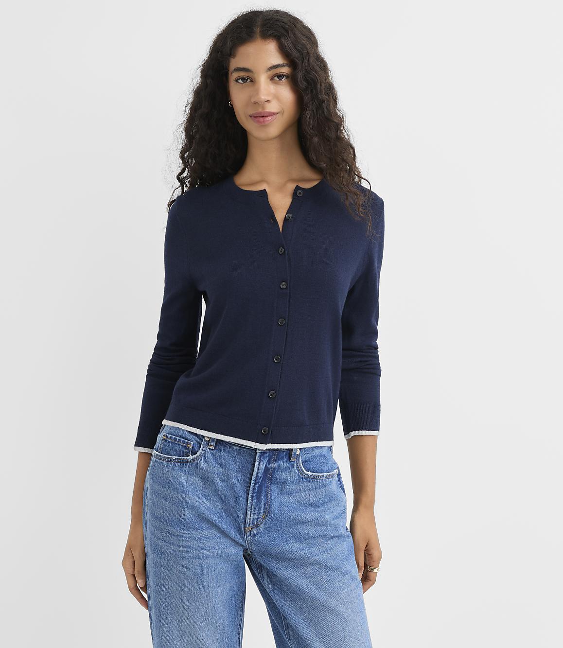 A woman in a navy cardigan and blue jeans stands against a plain white background.