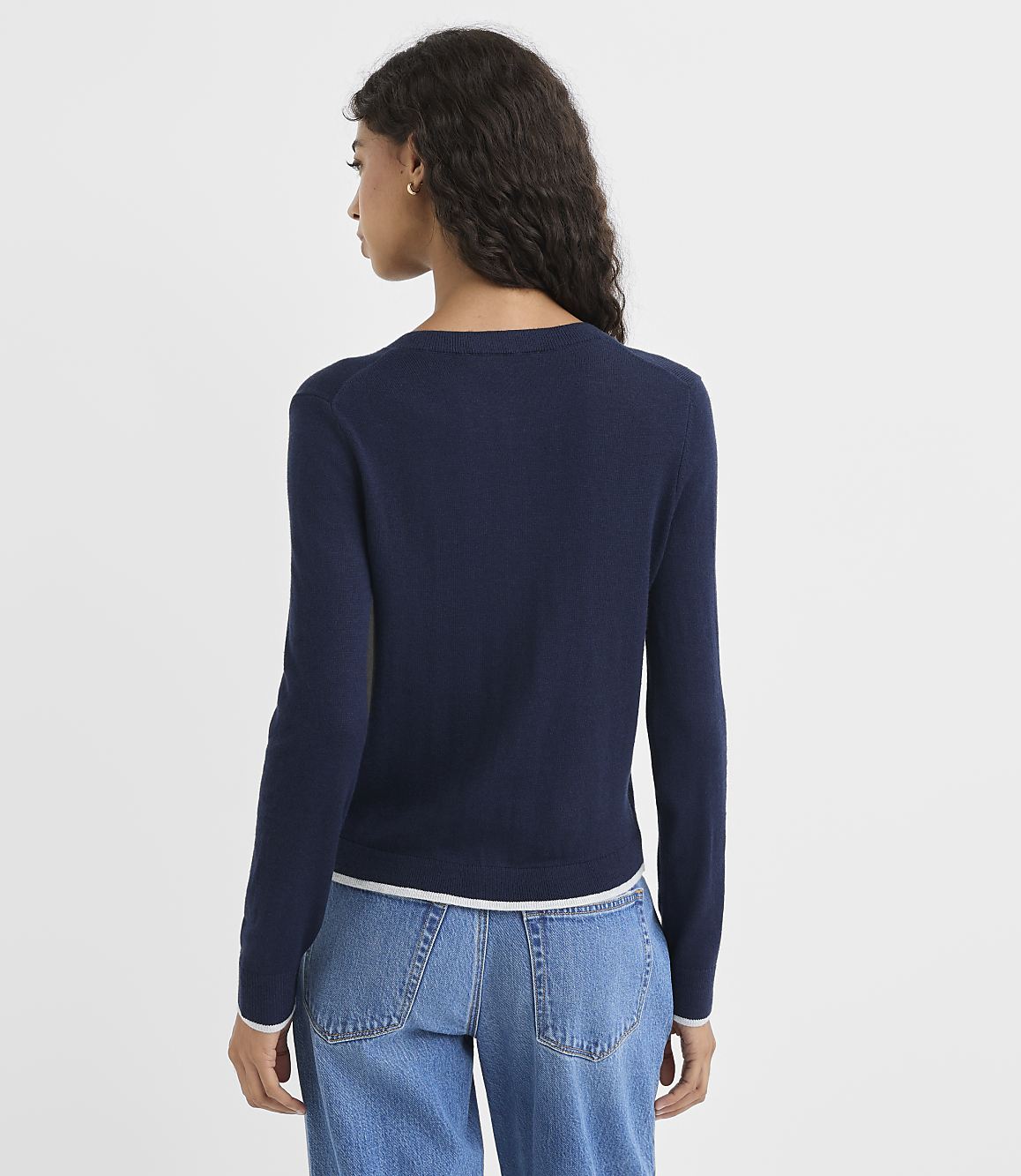 A woman in a navy sweater and jeans stands against a plain white background.