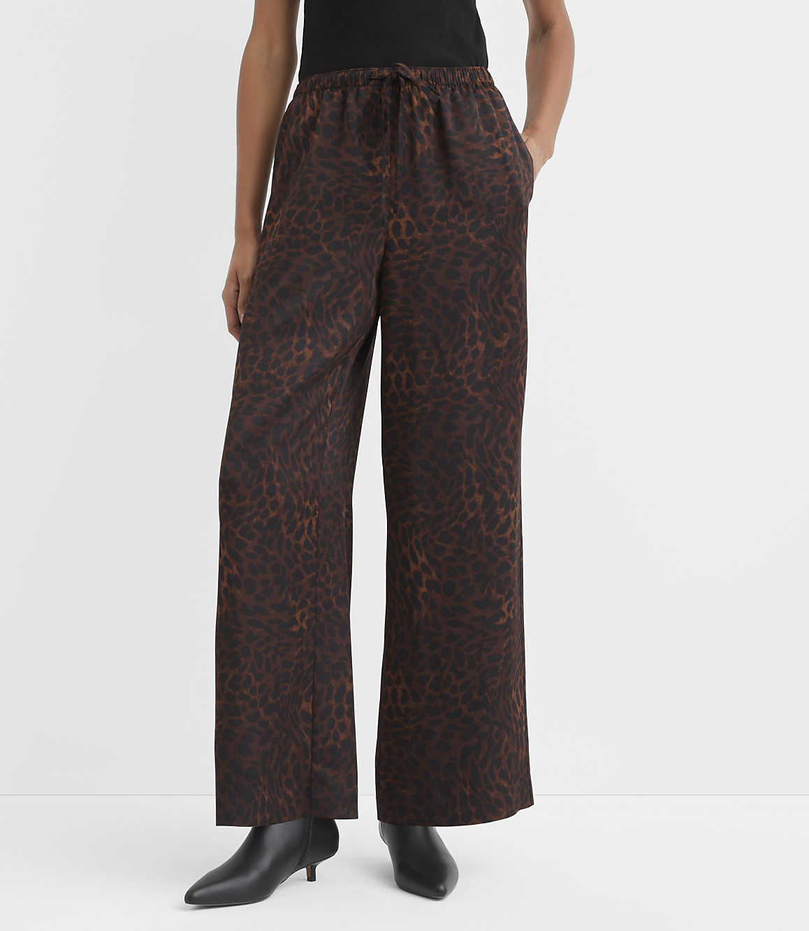 A person stands in wide-leg leopard print pants and black boots against a plain white background.