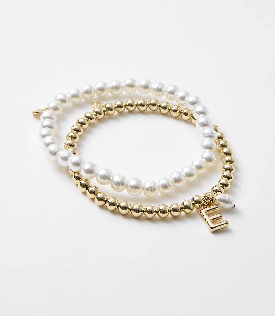 Two bracelets, one with pearls and the other with gold beads and an "E" charm, rest on a plain white background.