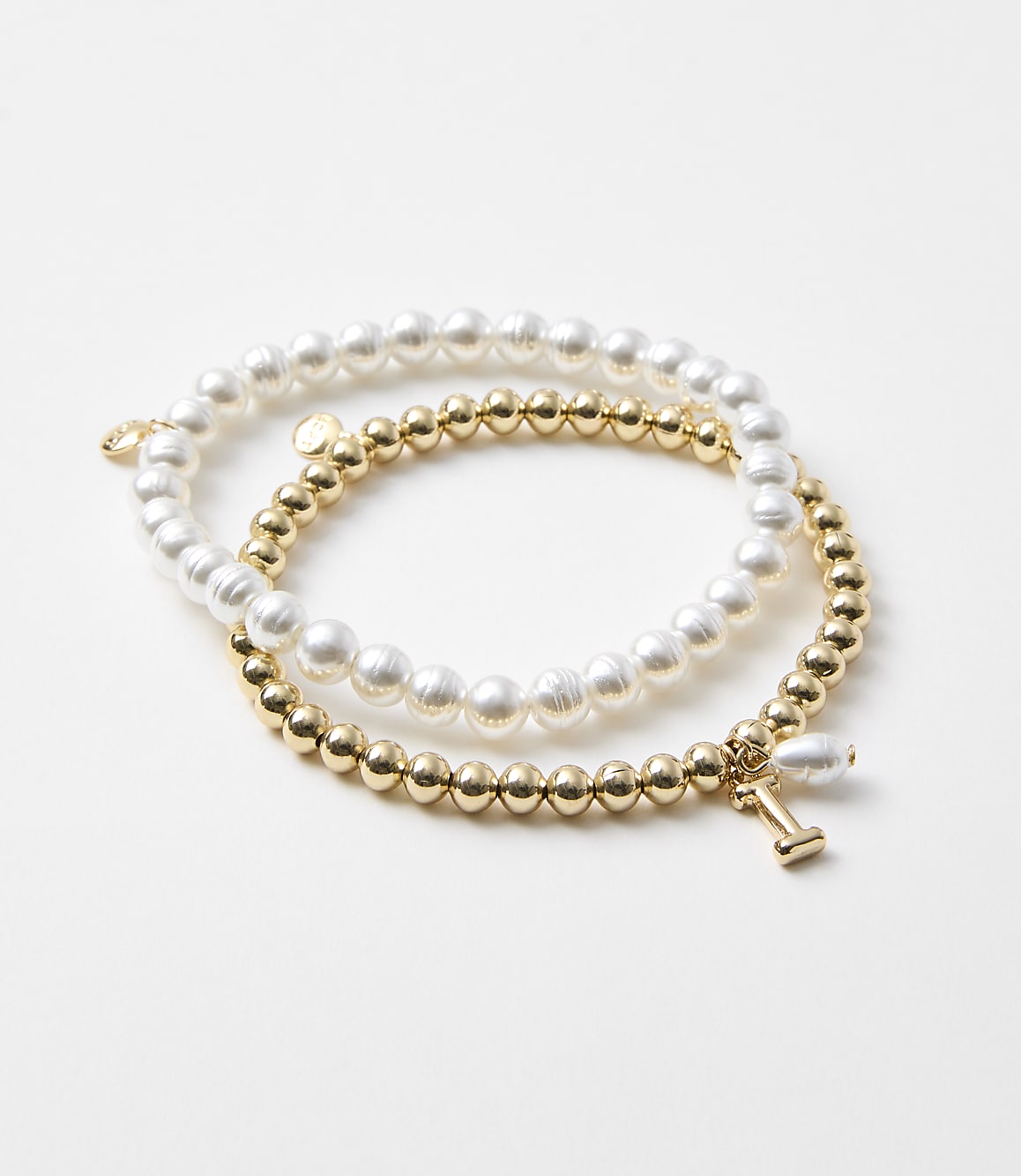 Two bracelets, one with pearls and the other with gold beads and a dumbbell charm, rest on a plain white background.