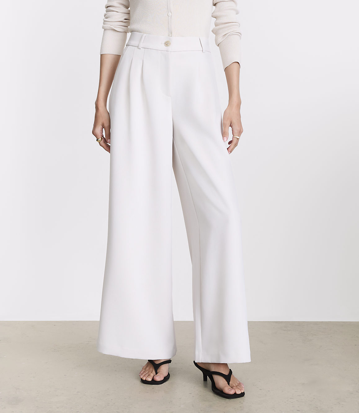 A person stands in wide-leg white pants and black heels against a plain white background.