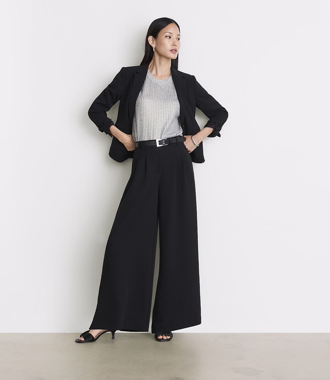 A woman in a black blazer and wide-leg pants stands against a plain white background.