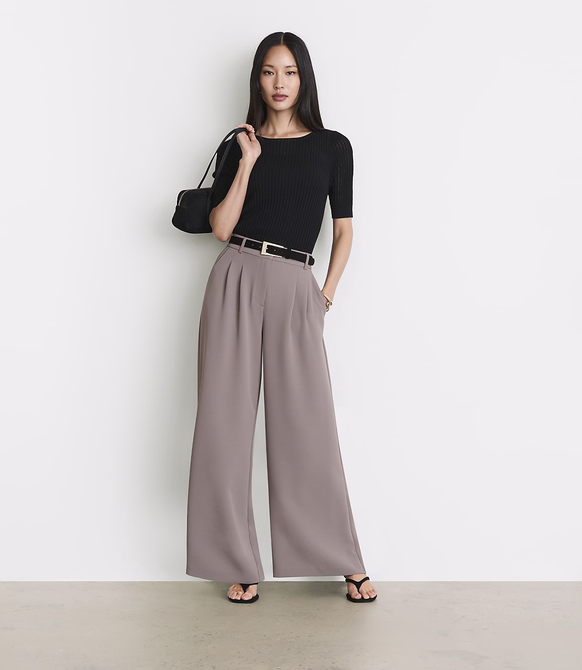 A woman in a black top and wide-leg pants stands against a plain white background.