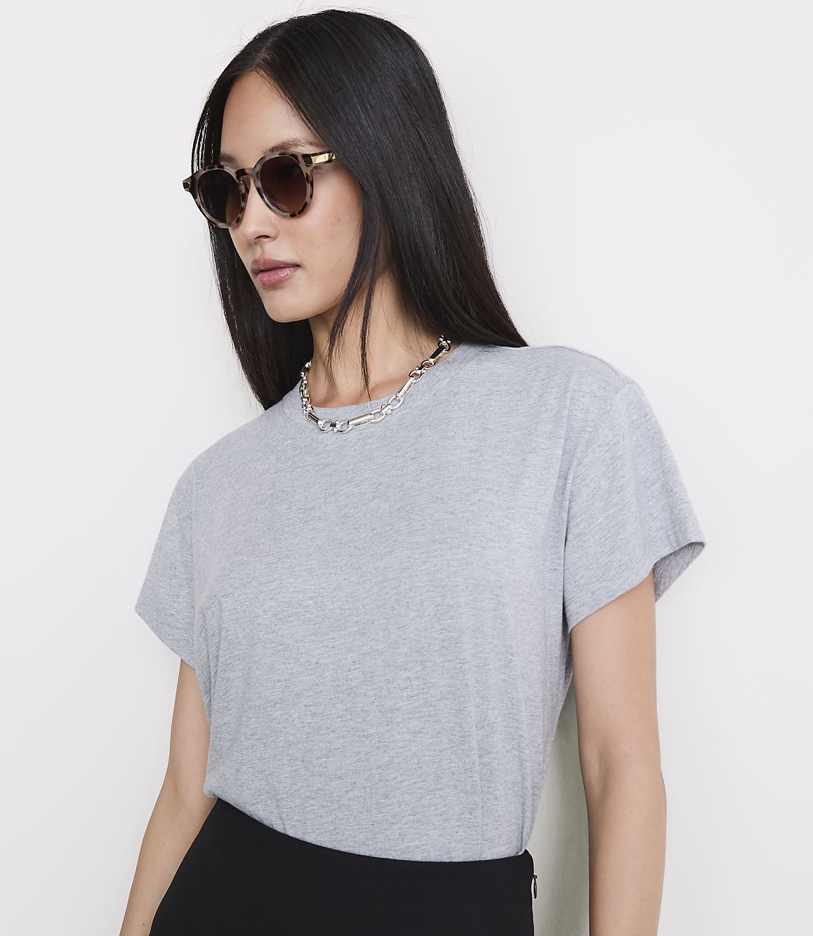 A woman in a grey t-shirt and sunglasses poses against a plain white background.