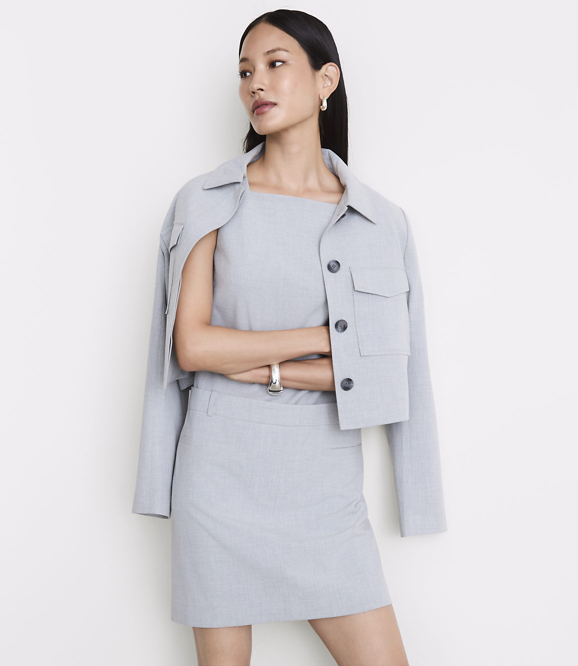 A woman in a light gray skirt suit stands with her arms crossed against a plain white background.