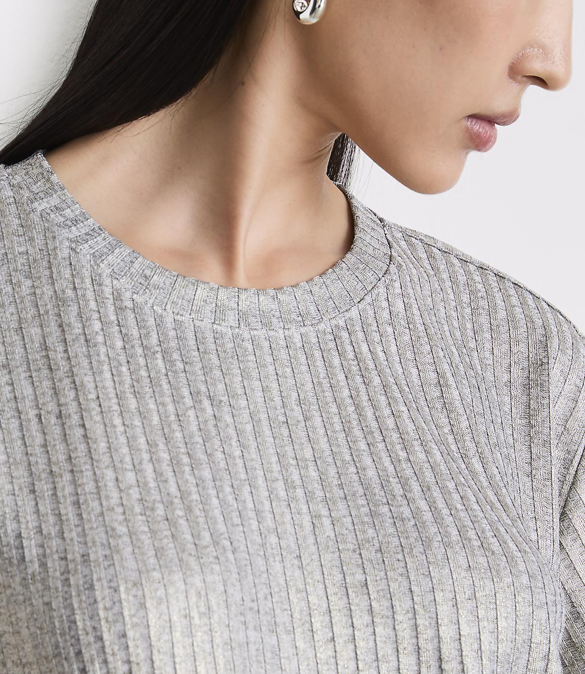 A woman's shoulder and neck are visible in the foreground, wearing a grey ribbed shirt, with a blurred background.