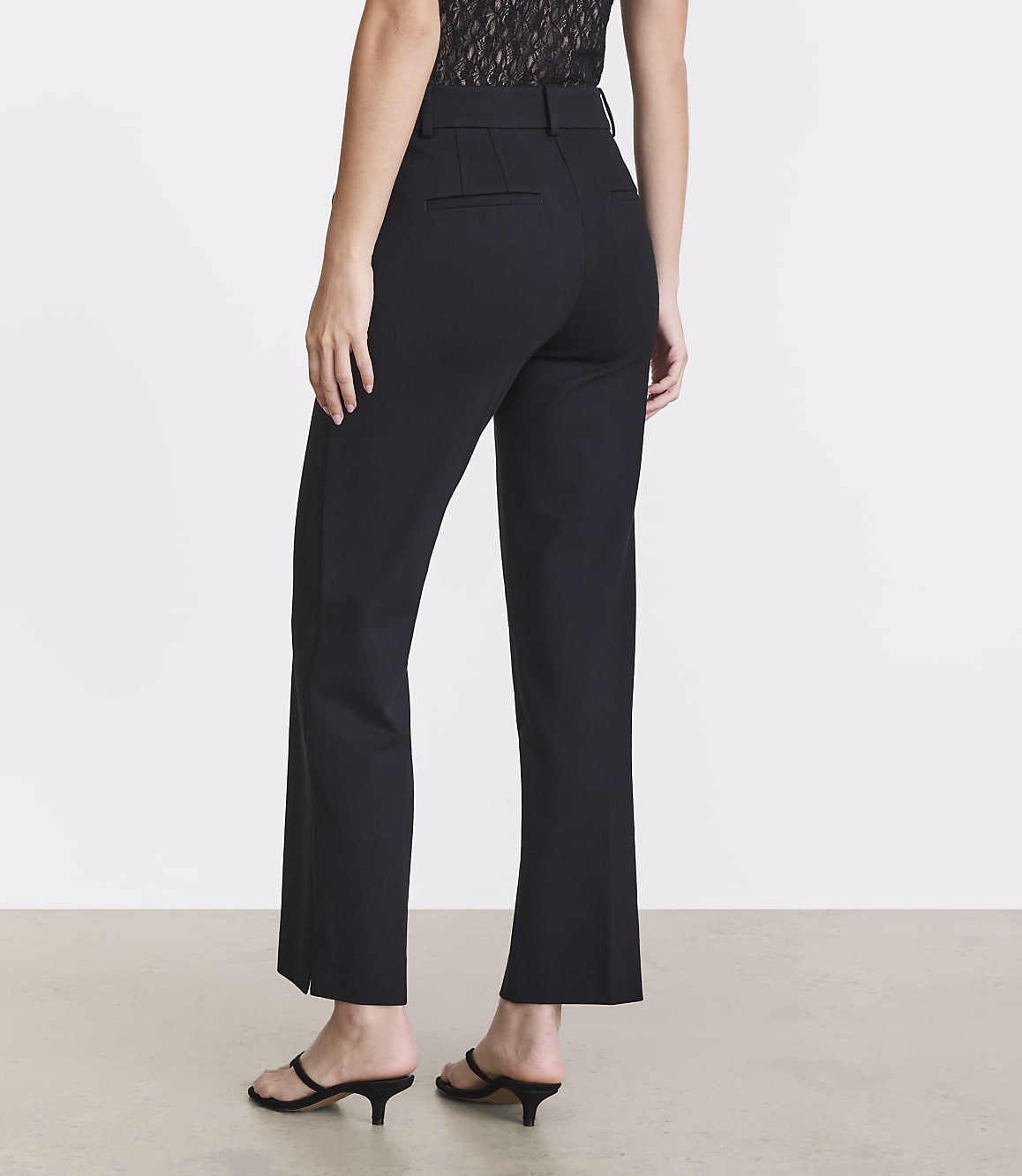 A person wearing black pants and black sandals stands against a plain white background.