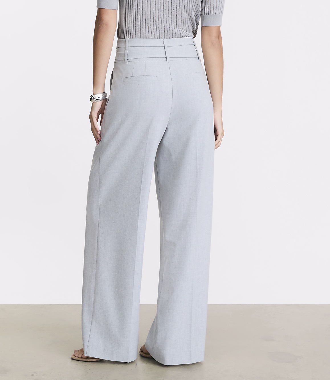 A person wearing light blue wide-leg pants and a grey ribbed top stands on a light-colored floor against a plain background.