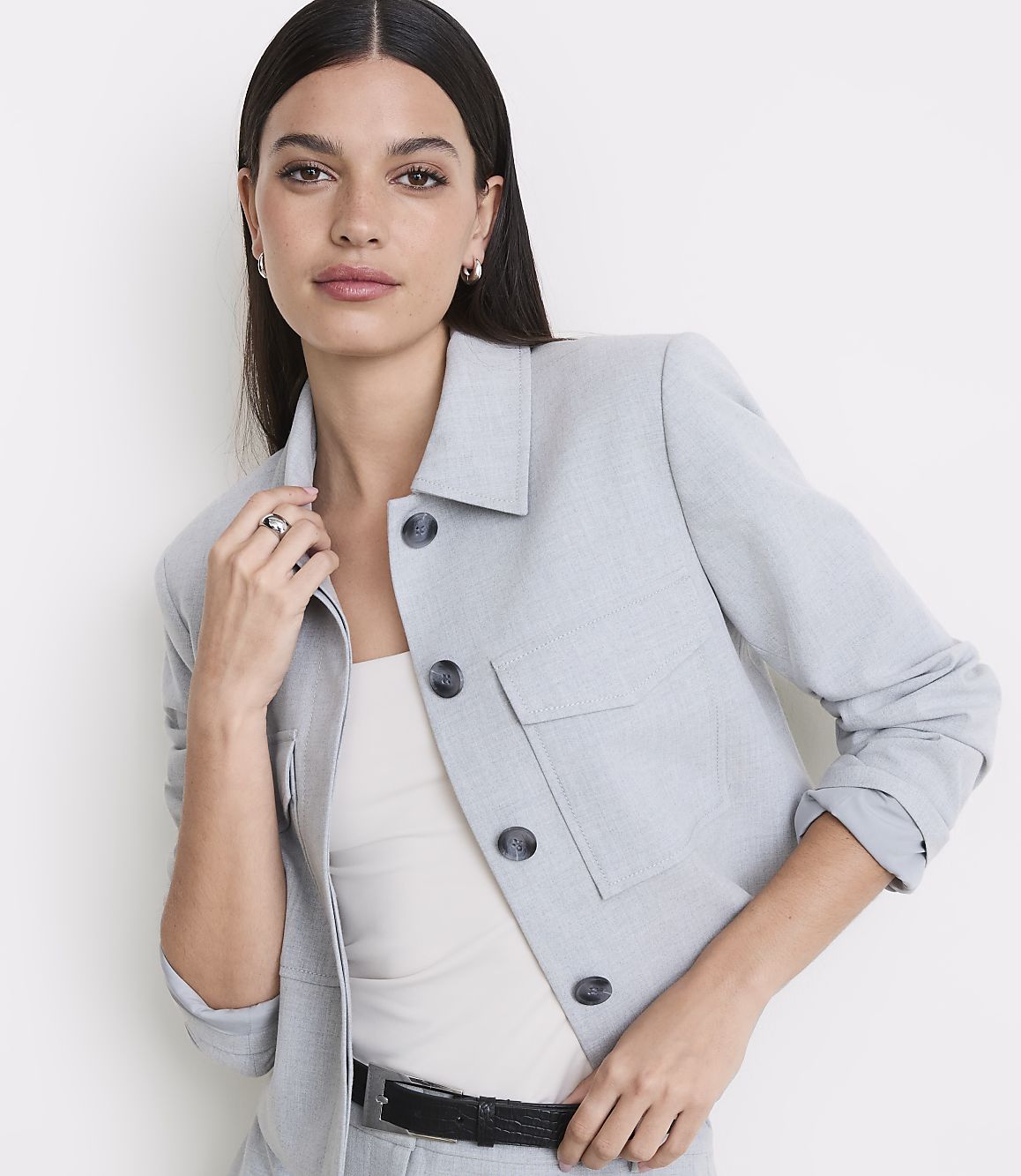 A woman in a light blue jacket and white top stands against a plain white background.
