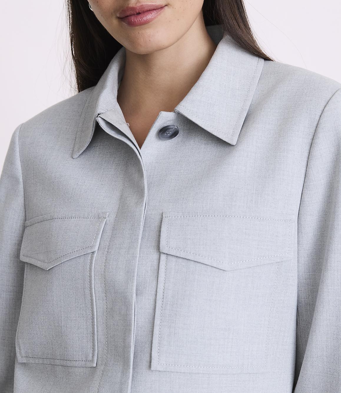 A woman in a light blue collared shirt with two chest pockets is shown from the chest up against a plain background.