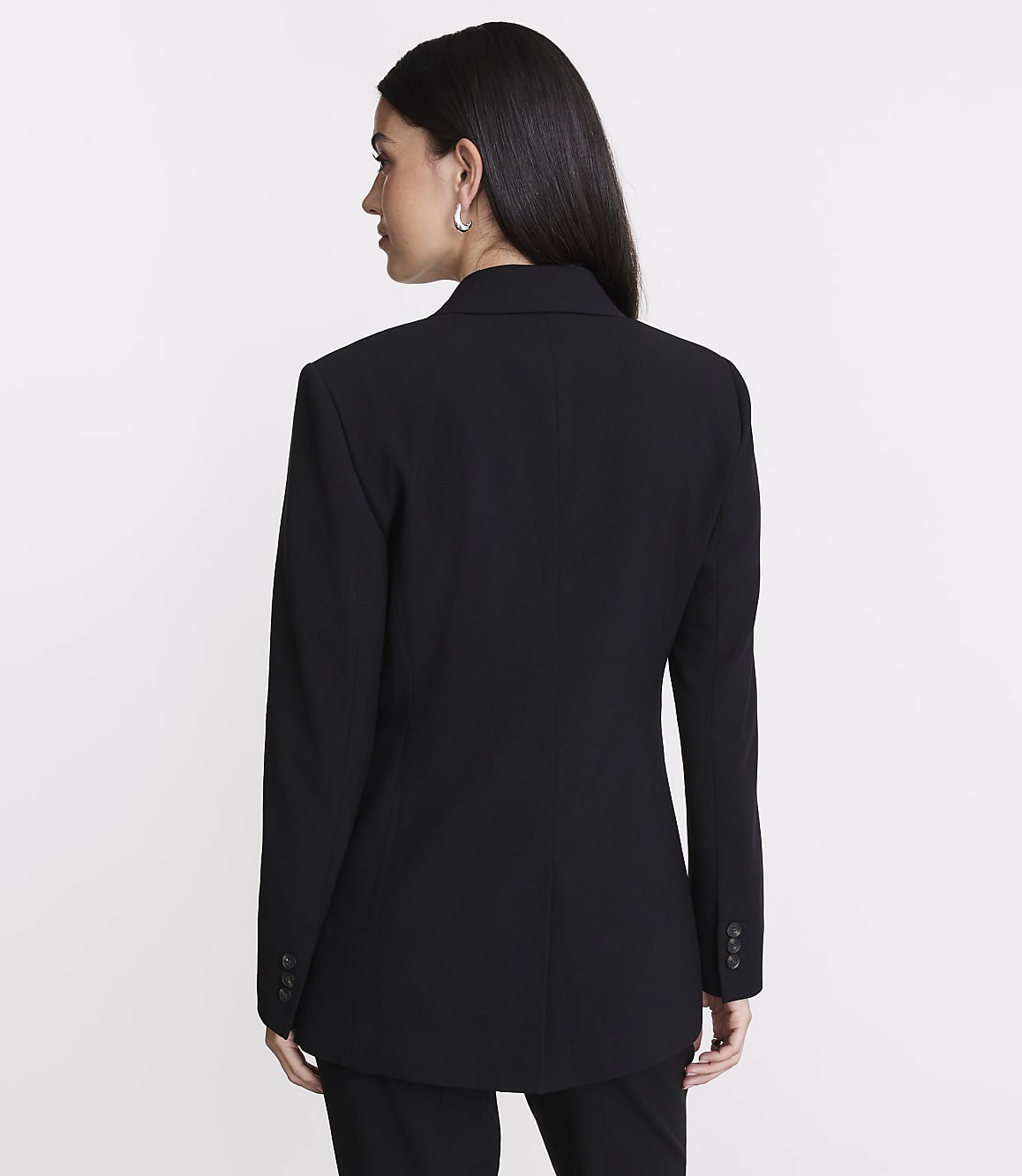 A woman in a black blazer stands against a plain white background.