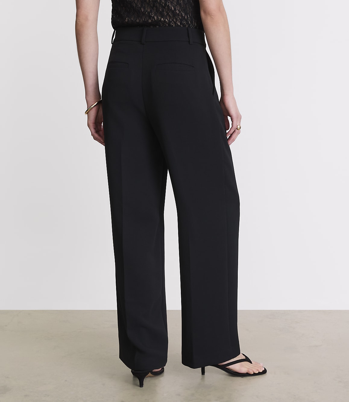 A person wearing black wide-leg pants and a patterned top stands against a plain, light-colored background.
