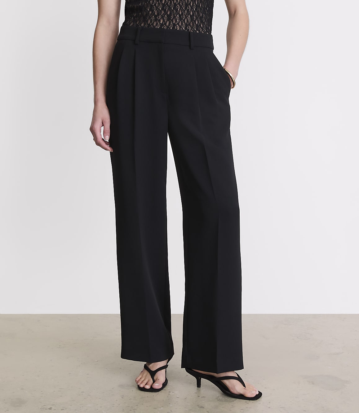 A person stands in black wide-leg trousers and sandals against a plain white background.