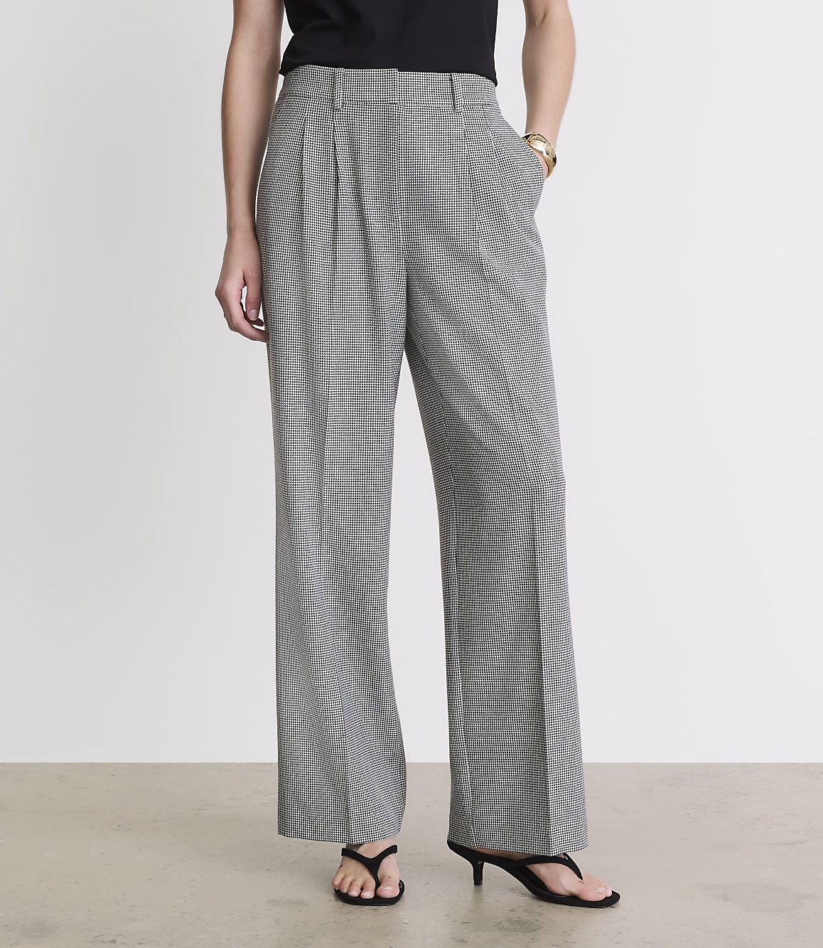 A person stands in front of a plain white background, wearing wide-leg, black and white patterned pants and black sandals.