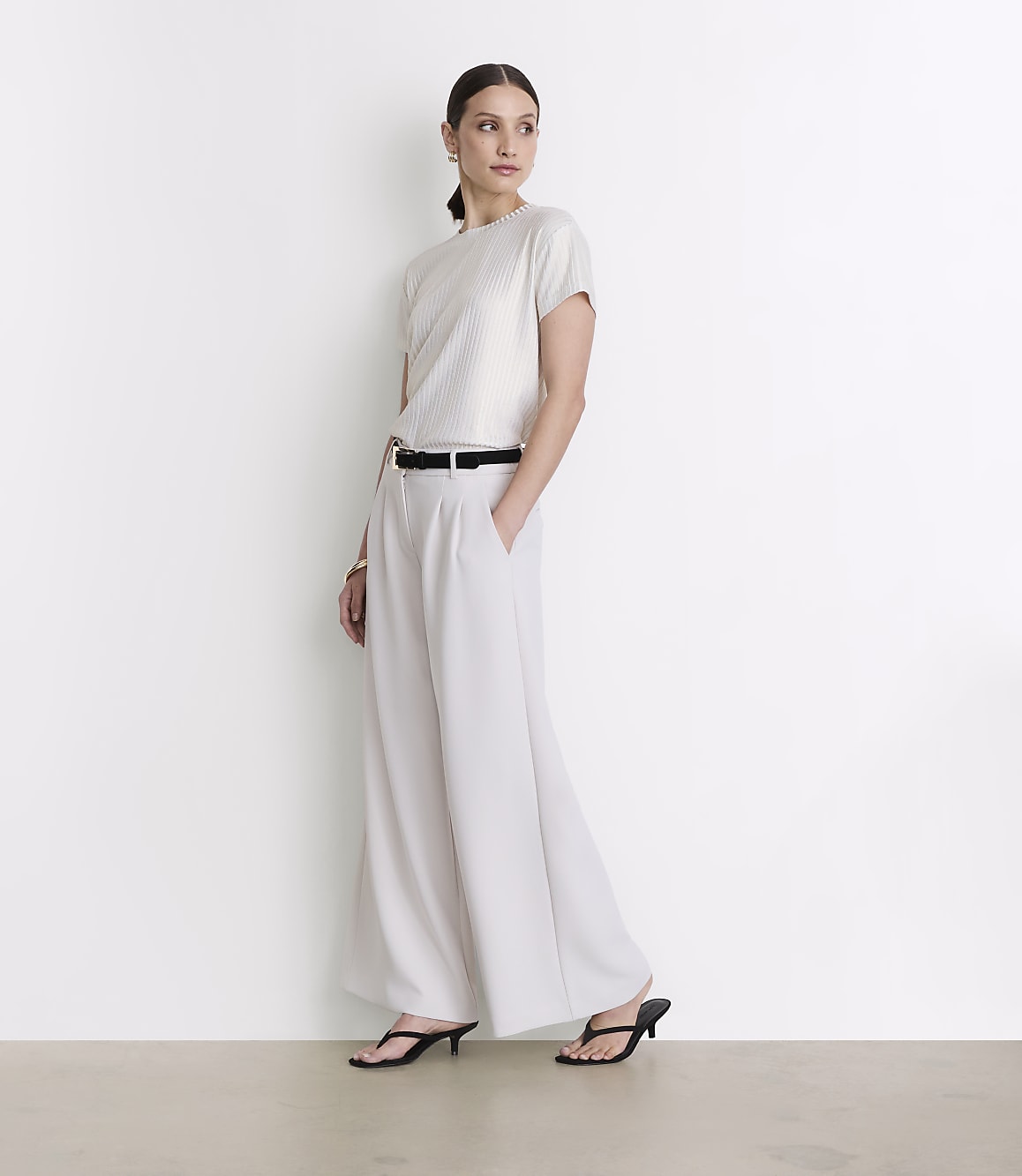 A woman in a white top and wide-leg pants stands against a plain white background.