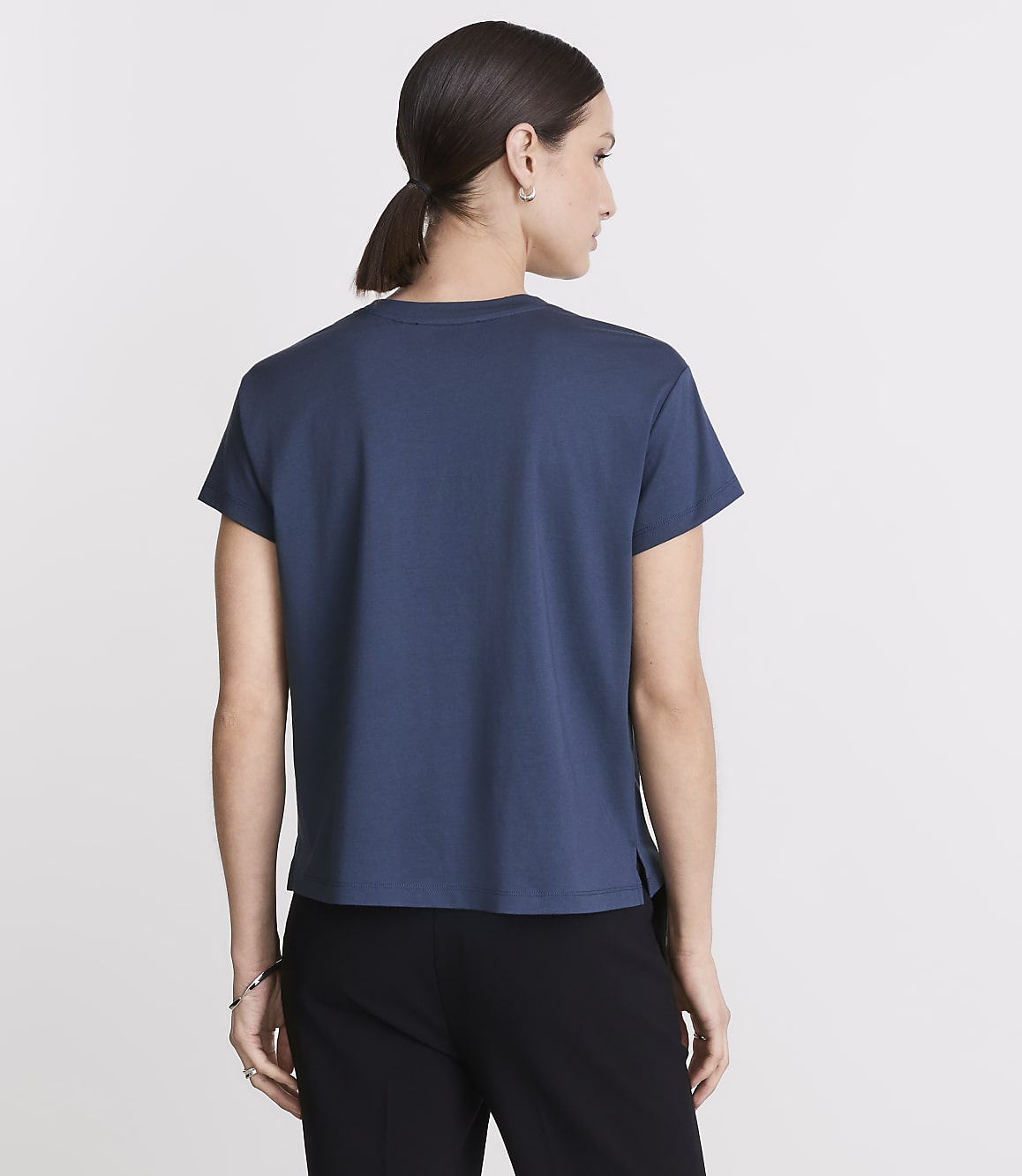 A woman in a blue t-shirt and black pants stands against a plain white background.