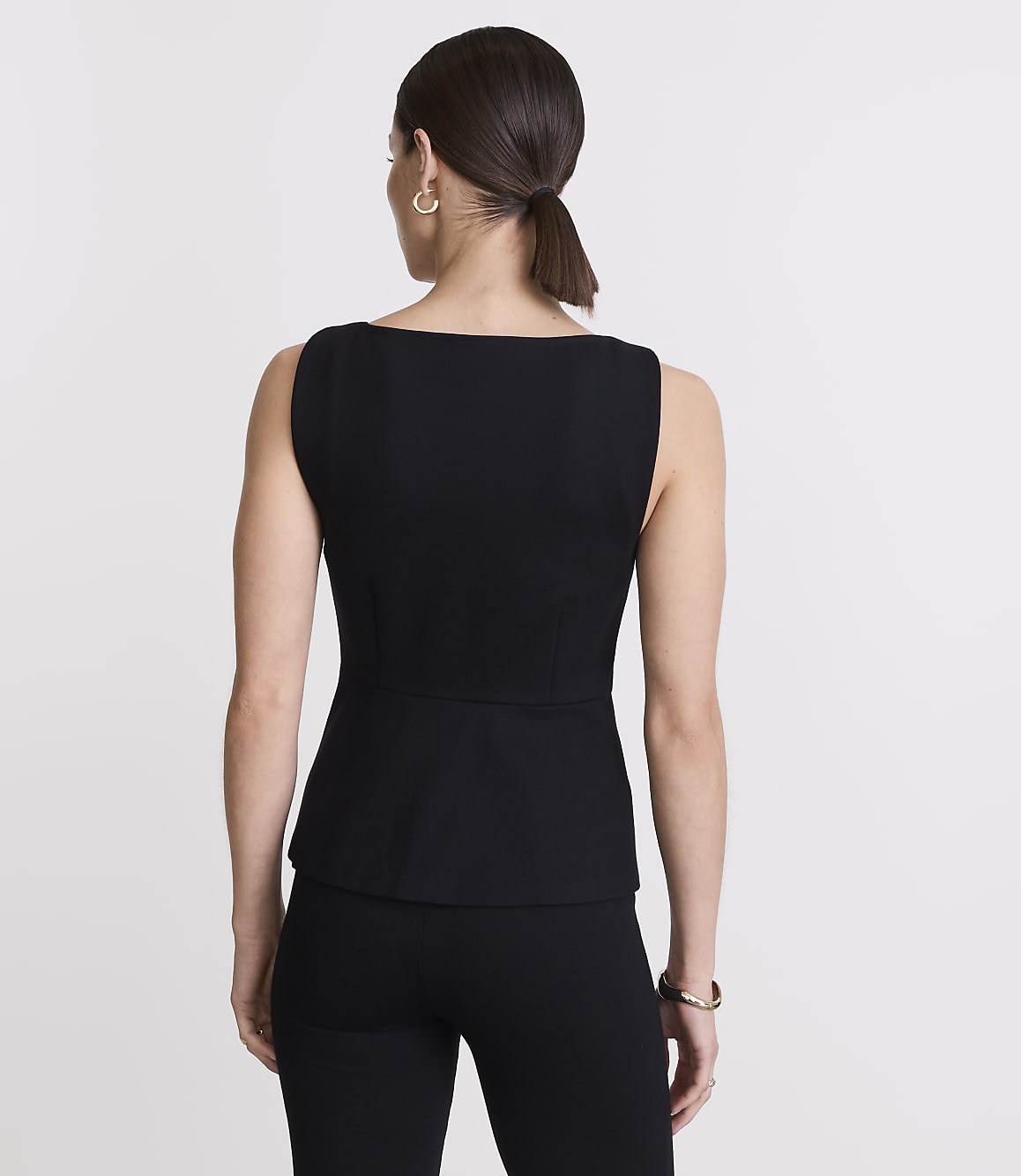 A woman in a black top and pants stands against a plain white background.