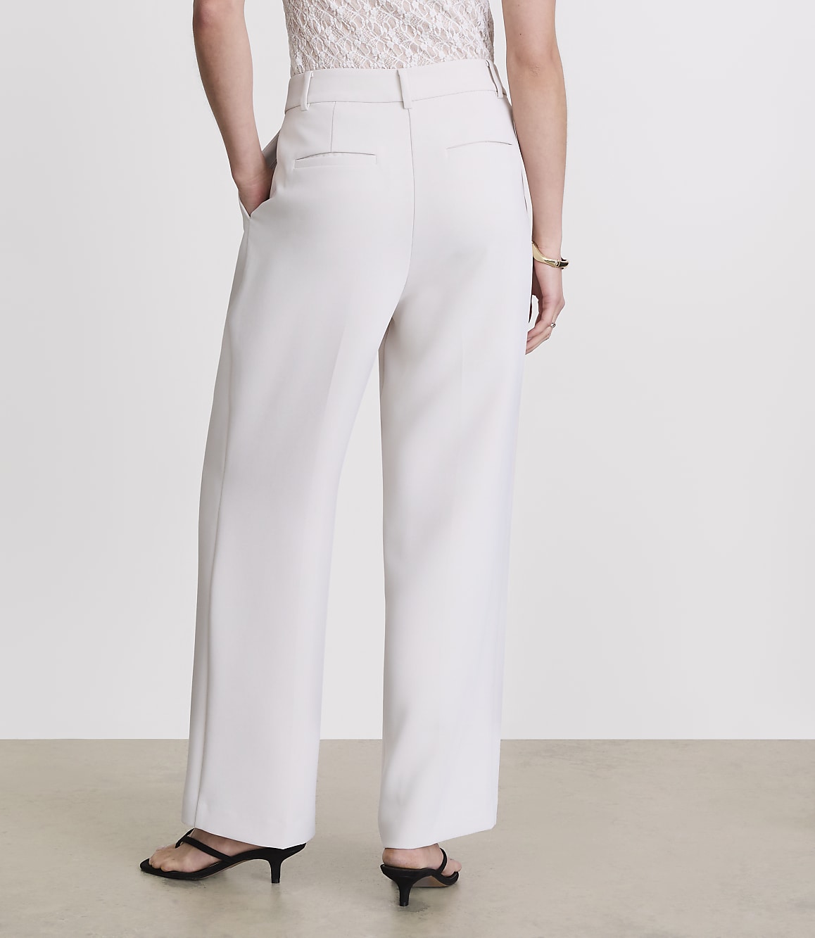 A person wearing cream-colored wide-leg pants and black heels stands against a plain white background.