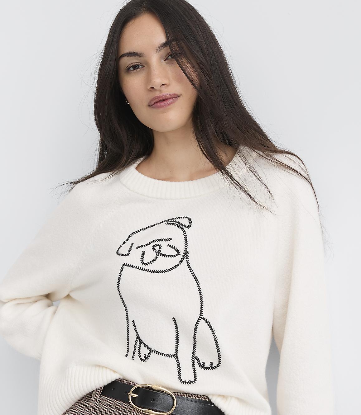 A woman in a cream sweater with a pug design stands against a plain white background.