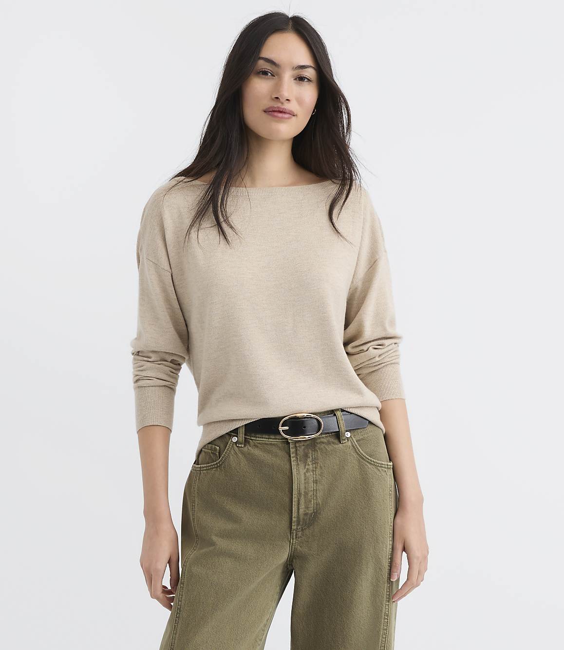 A woman in a beige sweater and green pants stands against a plain white background.