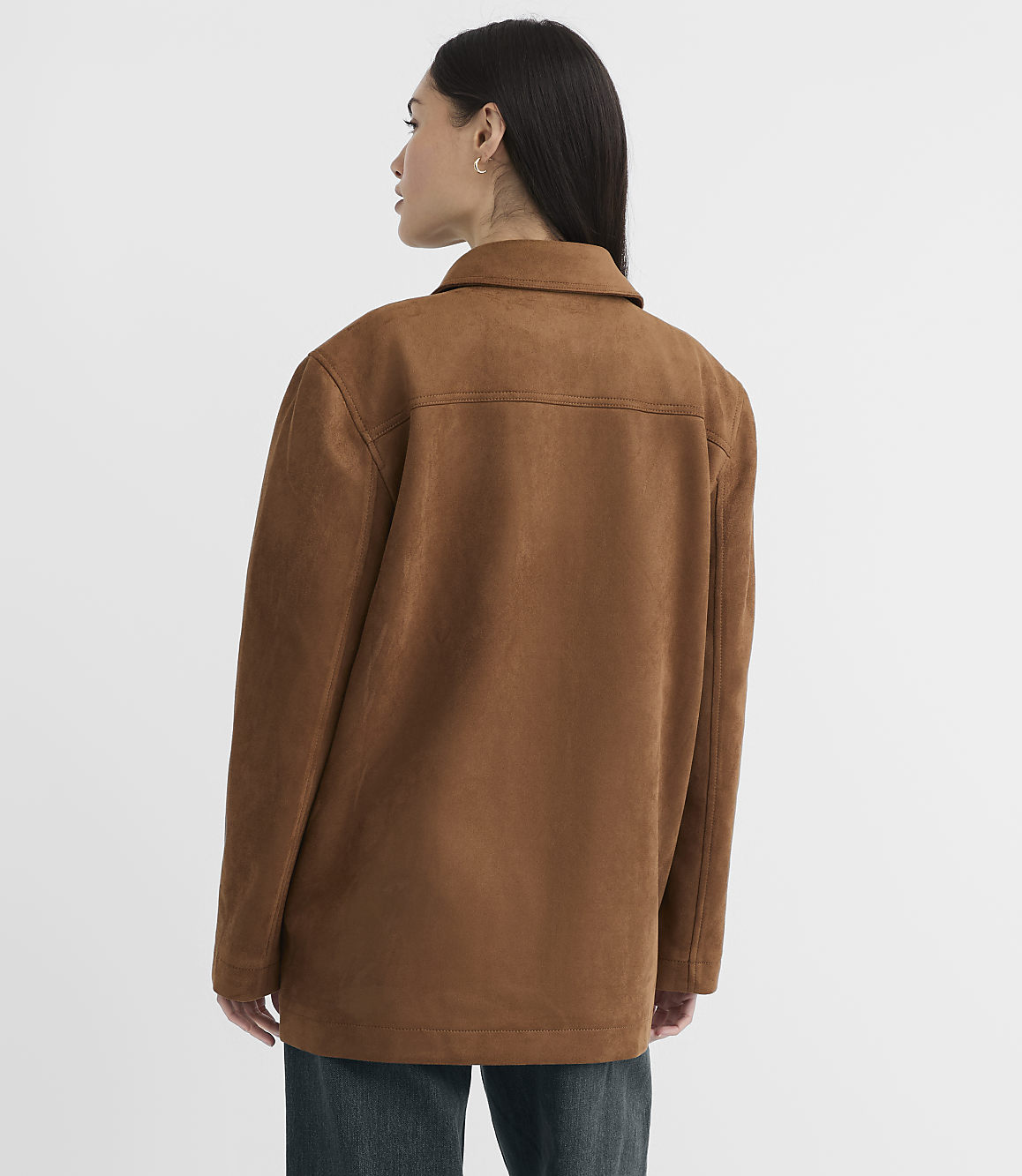 A woman in a brown suede jacket stands against a plain white background.