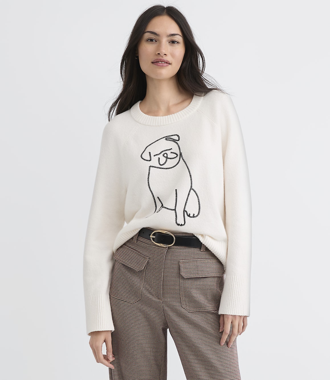 A woman in a cream sweater with a pug design stands against a plain white background.